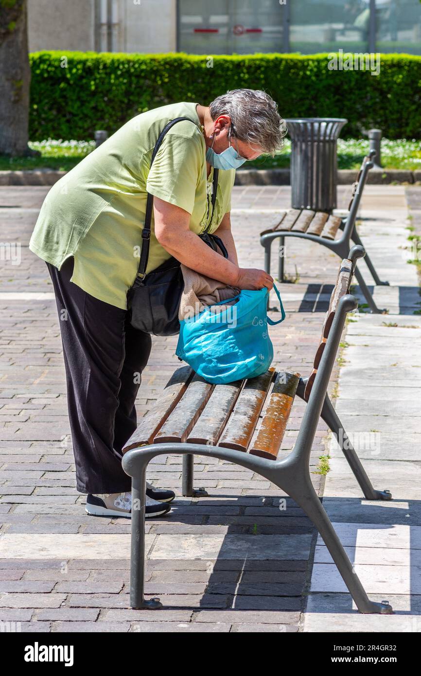 Frau mit Gesichtsmaske, die Einkaufstasche auf der Parkbank überprüft - Tours, Indre-et-Loire (37), Frankreich. Stockfoto
