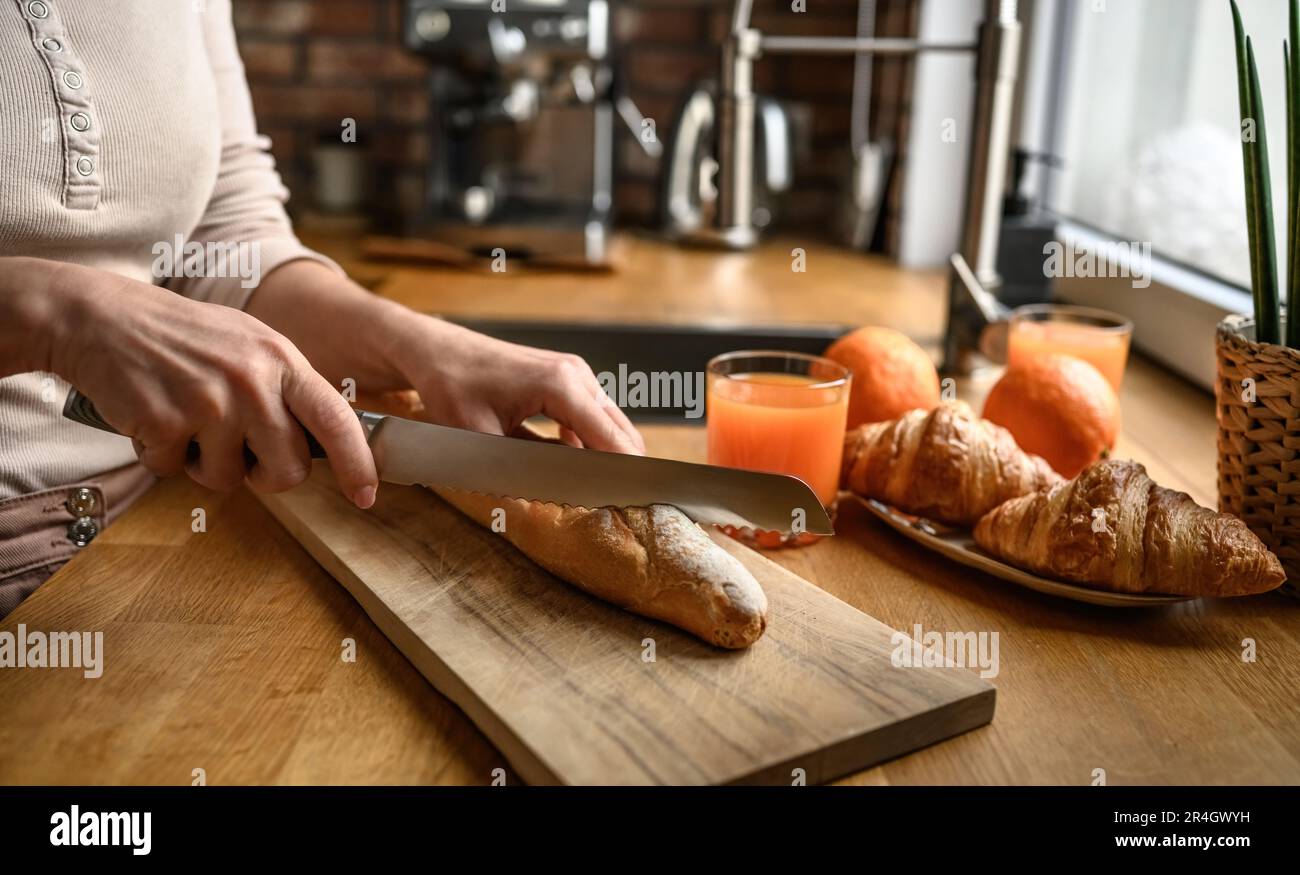 Ein Mädchen hat französisches Baguette mit Messer in der Küche geschnitten. Leckeres rustikales frisches Brot aus Frankreich zum Frühstück Stockfoto