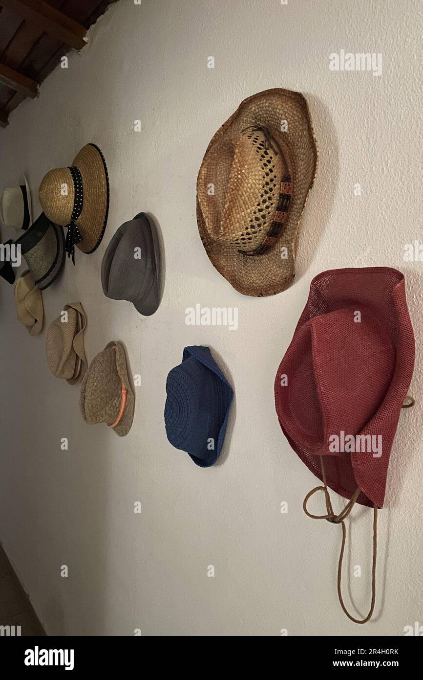 Hüte, die an einer weißen Wand in einem alten Saal mit Holzdecke hängen, hängende klassische, zeitlose Hüte für Männer und Frauen Stockfoto