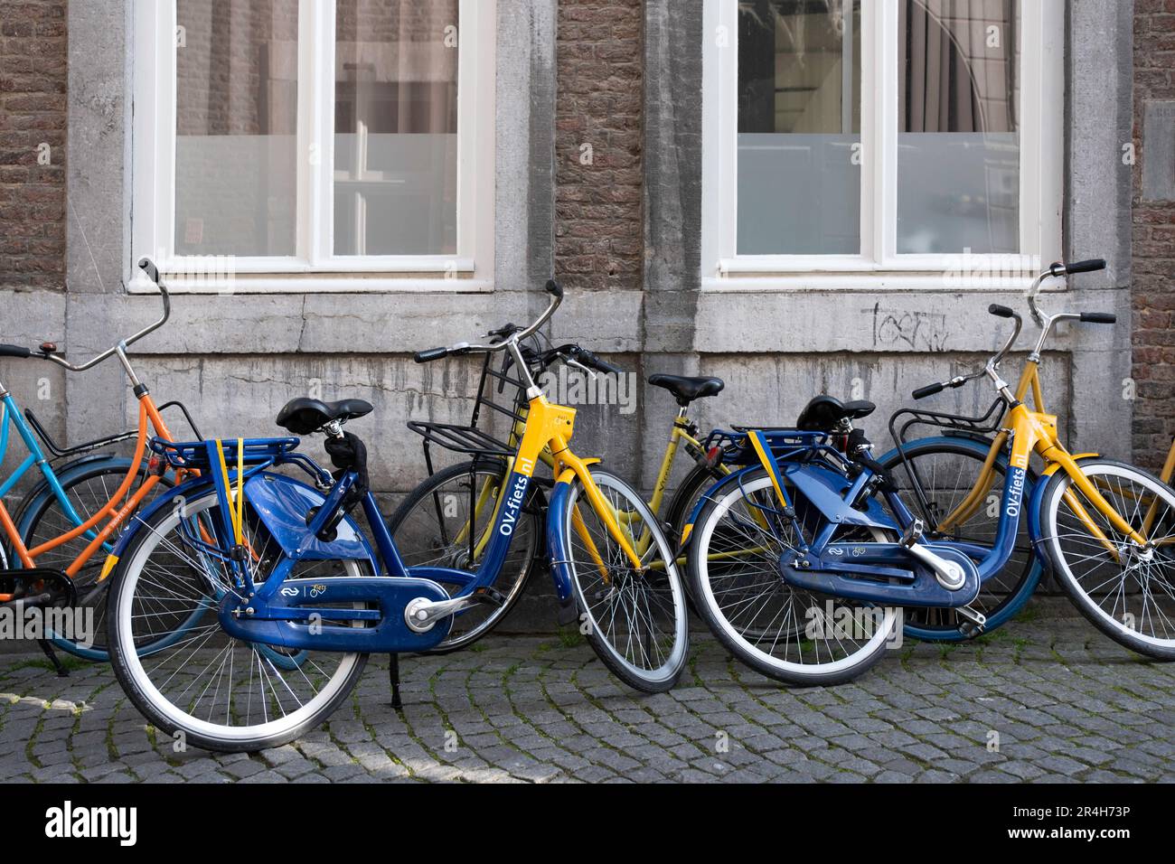 Ein paar blau-gelbe Leihfahrräder mit öffentlichen Verkehrsmitteln 'OV fietsen' stehen vor und vor einer Wand eines alten Gebäudes in Maastricht Stockfoto