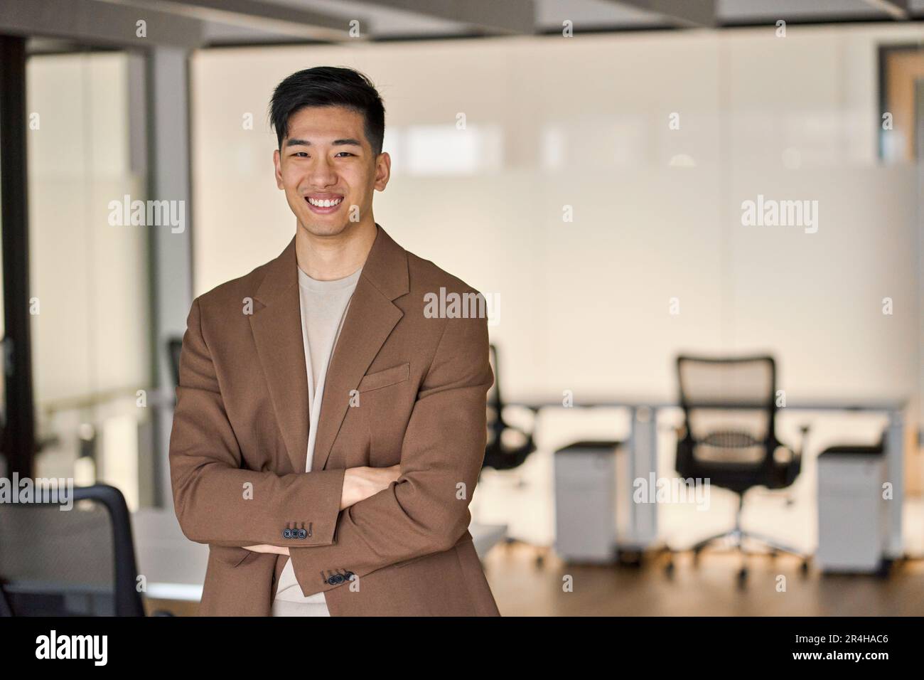 Junger, glücklicher asiatischer Geschäftsmann, der im Büro vor der Kamera steht. Porträt. Stockfoto
