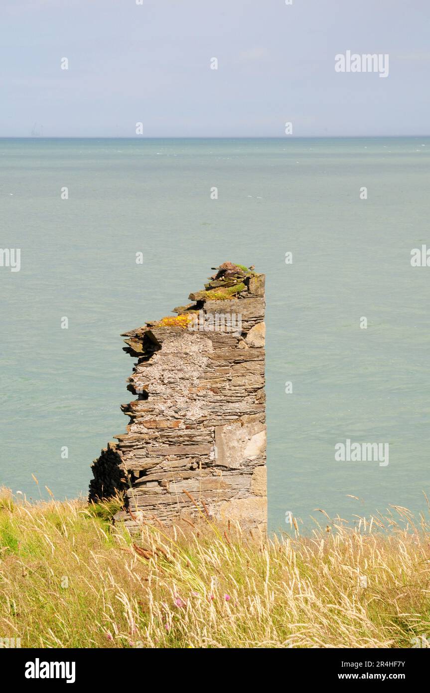 Ruiniertes Gebäude auf Klippen. Ostküste von Eire. Das Bohrfahrzeug ist gerade noch durch den Dunst am Horizont sichtbar. Stockfoto