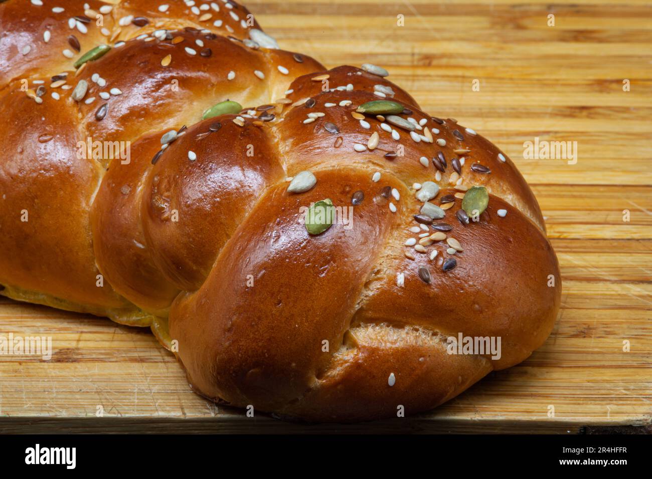 Ein weißer Challah-Laib auf einem Holzbrett mit Leinsamen, Sonnenblumenkernen und Kürbiskernen. Frisch gebackene goldene Kruste mit Highlights. Stockfoto