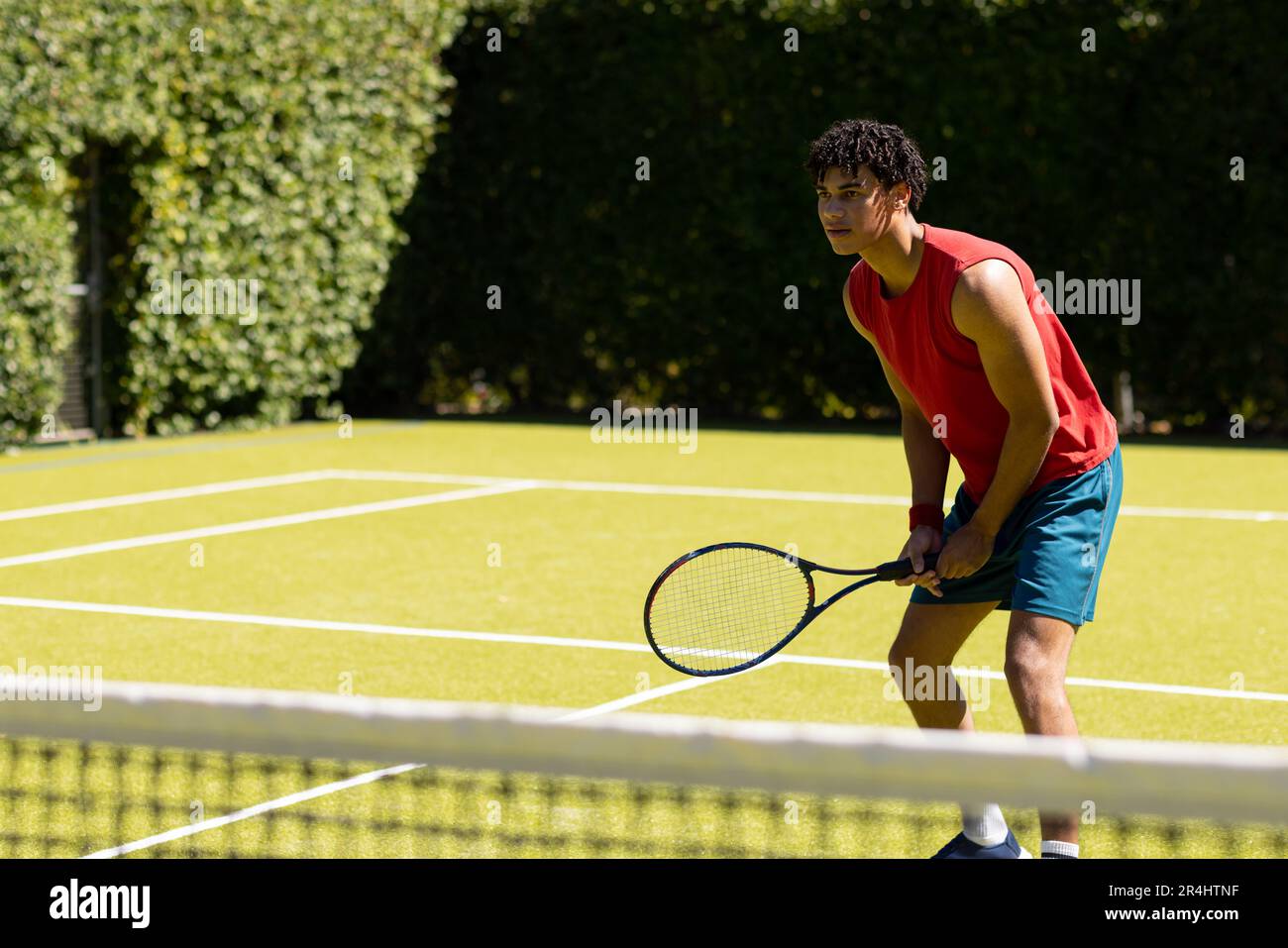 Ein birassischer junger Mann, der Tennisschläger hält und auf einem Wiesenfeld auf dem Tennisplatz steht Stockfoto