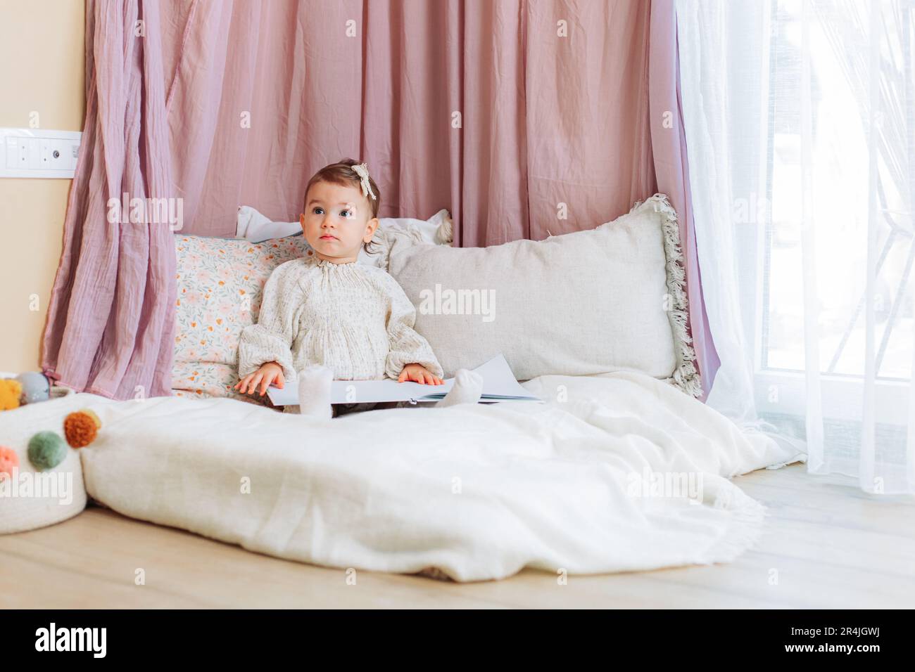 Süßes kleines Mädchen, das auf den Kissen sitzt und ein Buch liest Stockfoto