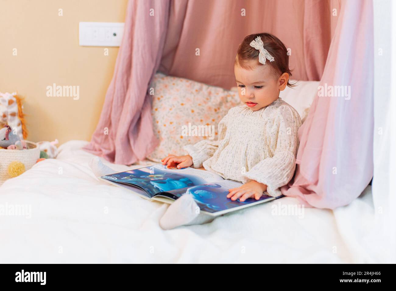 Süßes kleines Mädchen, das auf den Kissen sitzt und ein Buch liest Stockfoto