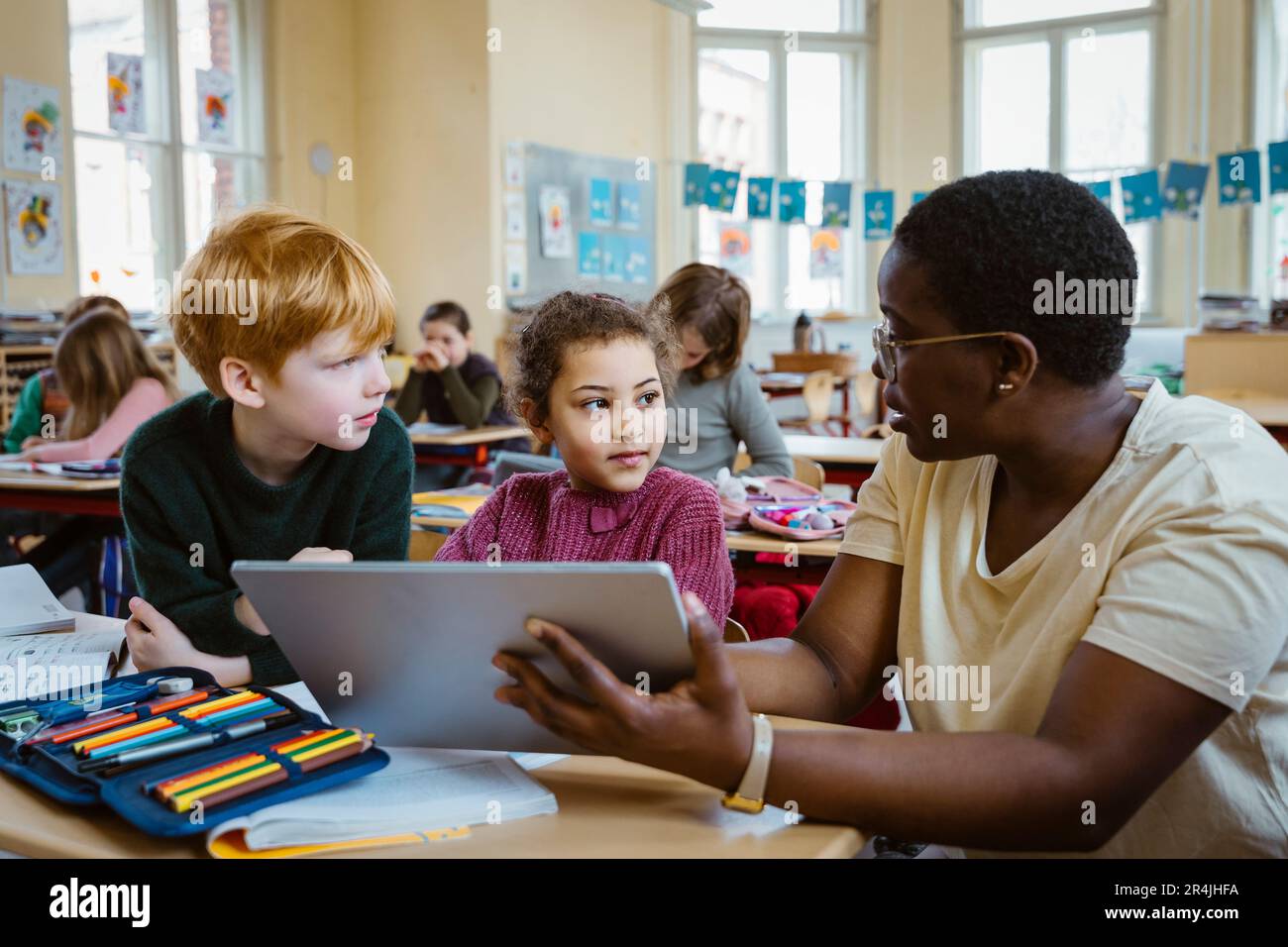 Lehrerin, die Schuljunge und Schulmädchen mit einem digitalen Tablet im Klassenzimmer unterstützt Stockfoto