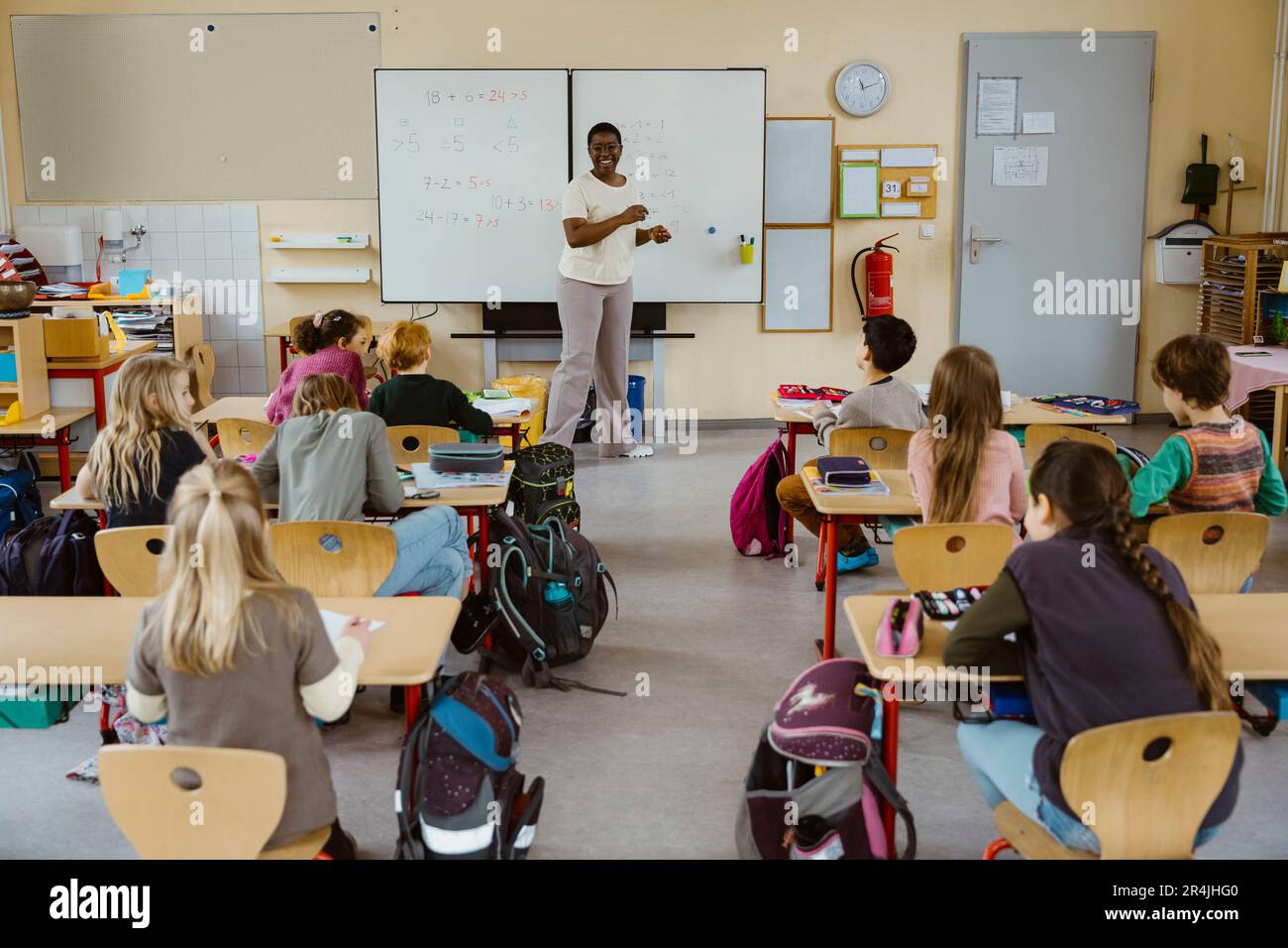 Glückliche Lehrerin, die mit Schülern im Klassenzimmer gegen das Whiteboard steht Stockfoto