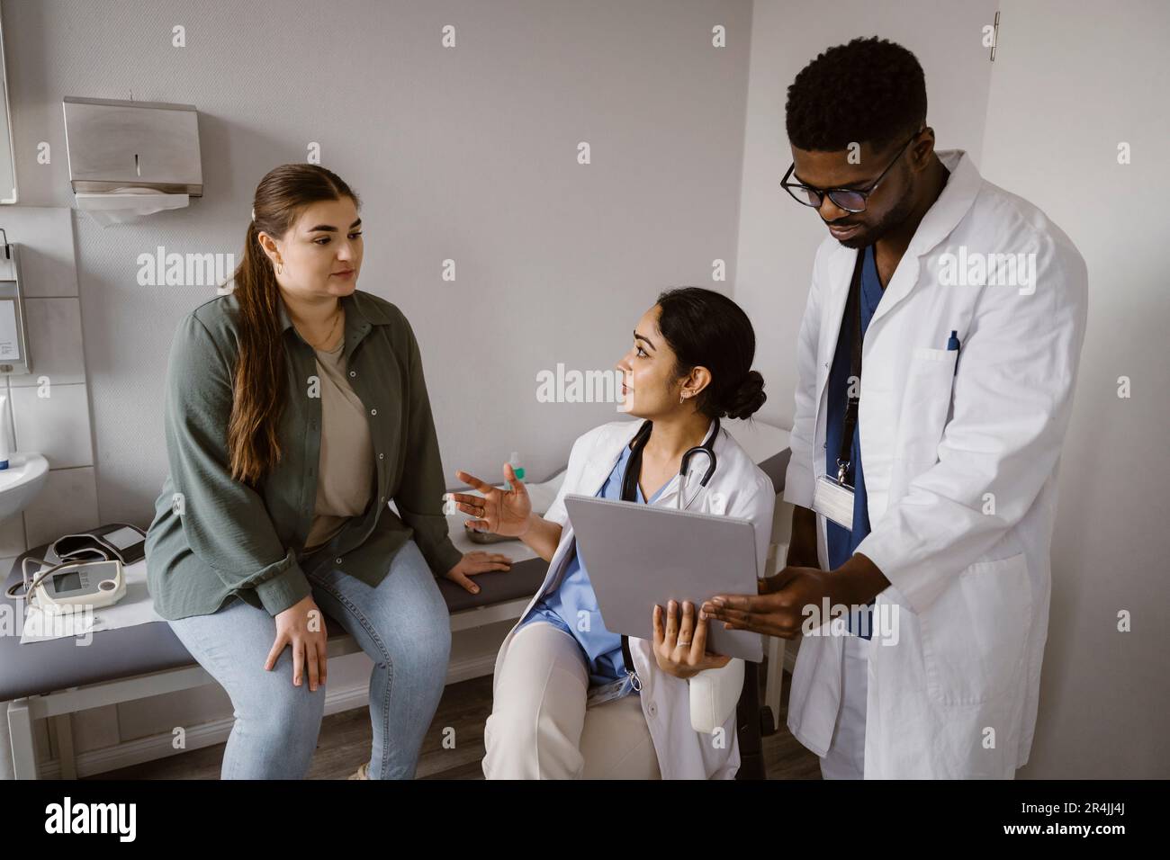 Arzt hält Tablet-PC und spricht mit einer Patientin, die in der Klinik im Bett sitzt Stockfoto