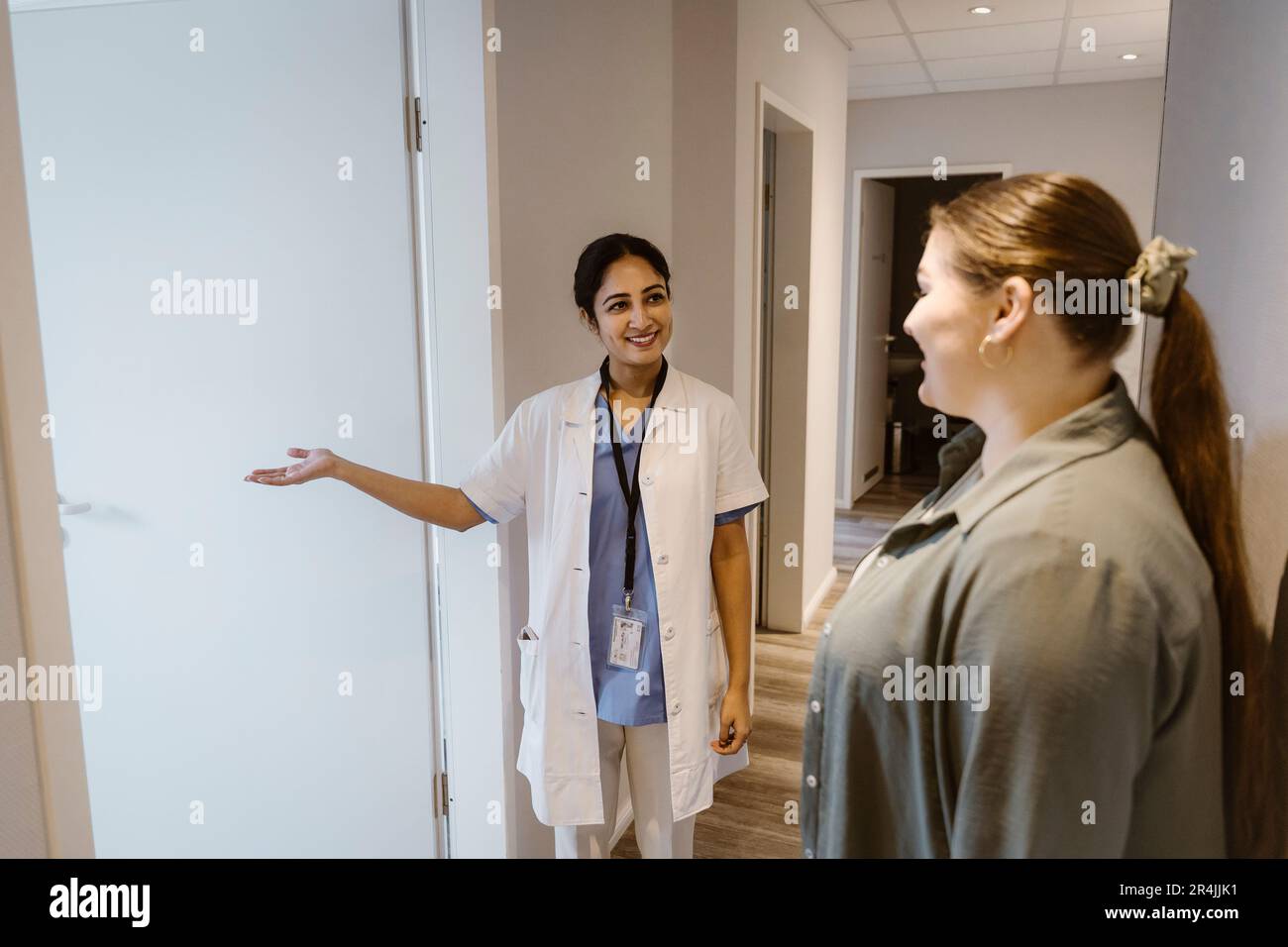 Lächelnder Arzt, der eine Patientin in den medizinischen Untersuchungsraum der Klinik bringt Stockfoto