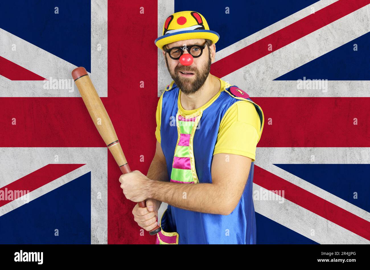 Ein unsicherer Clown hält eine Fledermaus in seinen Händen vor dem Hintergrund der britischen Flagge. Stockfoto