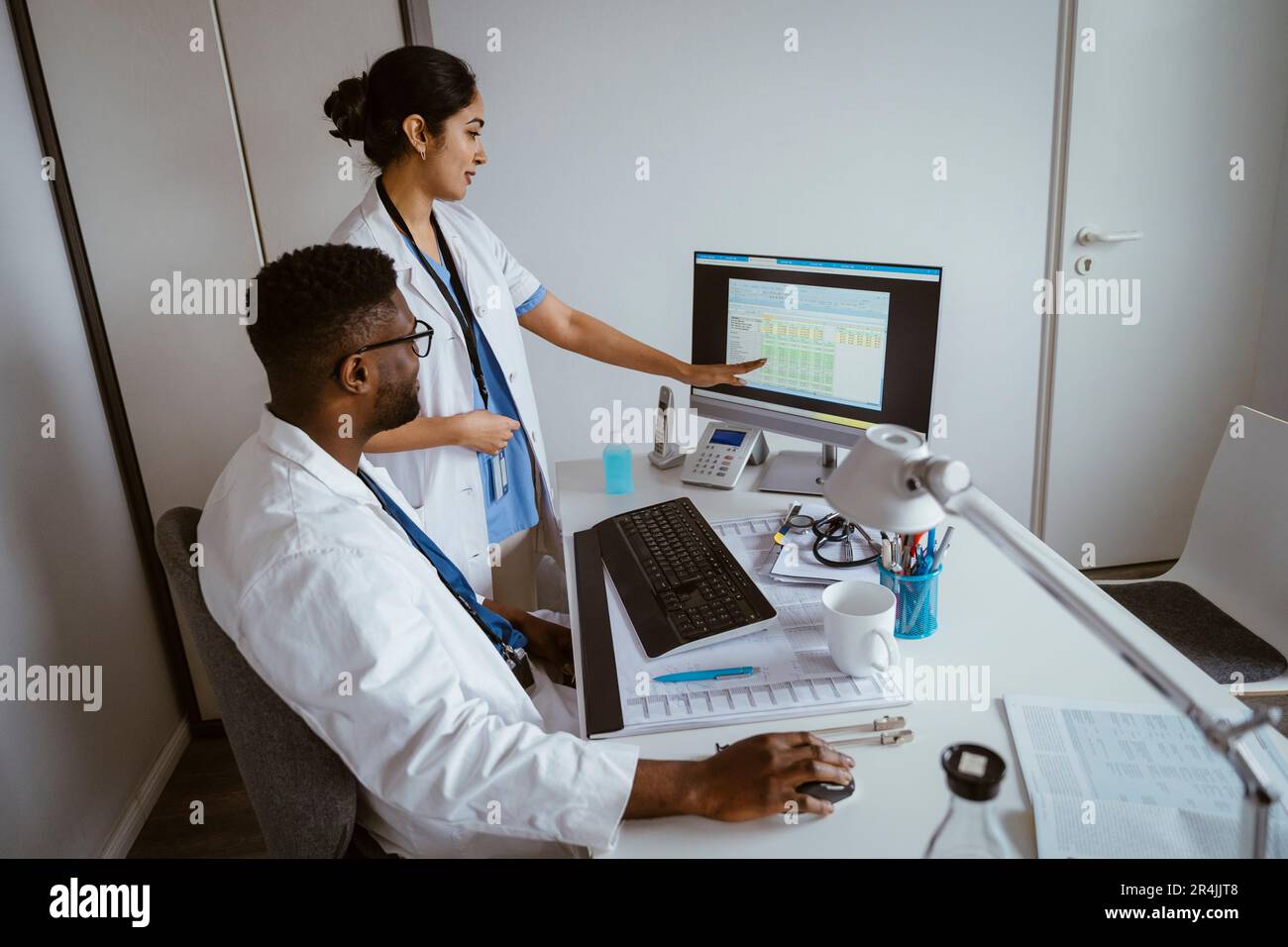 Ärztin erklärt dem männlichen Kollegen Strategie über Desktop-PC im Gesundheitszentrum Stockfoto