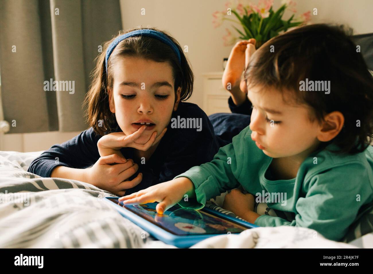 Brüder, die ein digitales Tablet benutzen, während sie zu Hause im Bett liegen Stockfoto