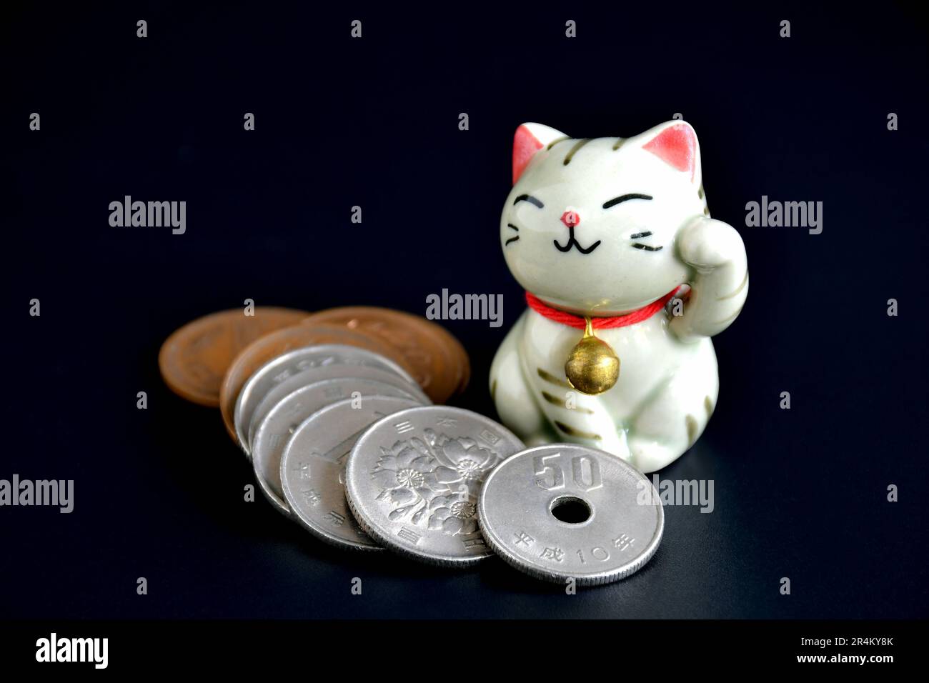 Geschlossen von winzigen handgemachten Töpfern von Maneki-Neko, der Glückskatze und japanischem Geld auf dunklem Hintergrund. Stockfoto