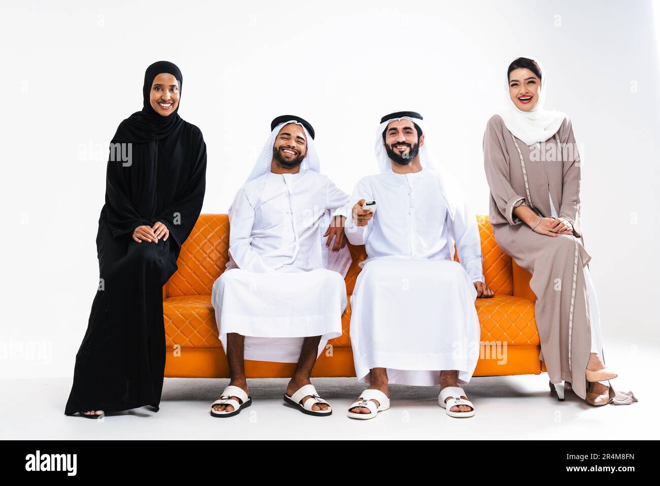 Wunderschöne arabische, glückliche Gruppe von Freunden, die zu Hause traditionelle Abaya- und Kandora-Verbindungen tragen - arabisch-muslimische Erwachsene Leute, die auf dem sitzen Stockfoto