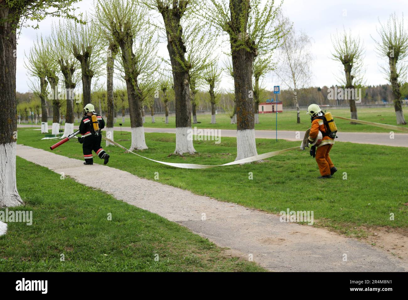 Professionelle Feuerwehrleute, Retter in feuerfesten Schutzanzügen, Helme und Gasmasken fliehen mit einem Feuerwehrschlauch, einem Wasserschlauch. Stockfoto