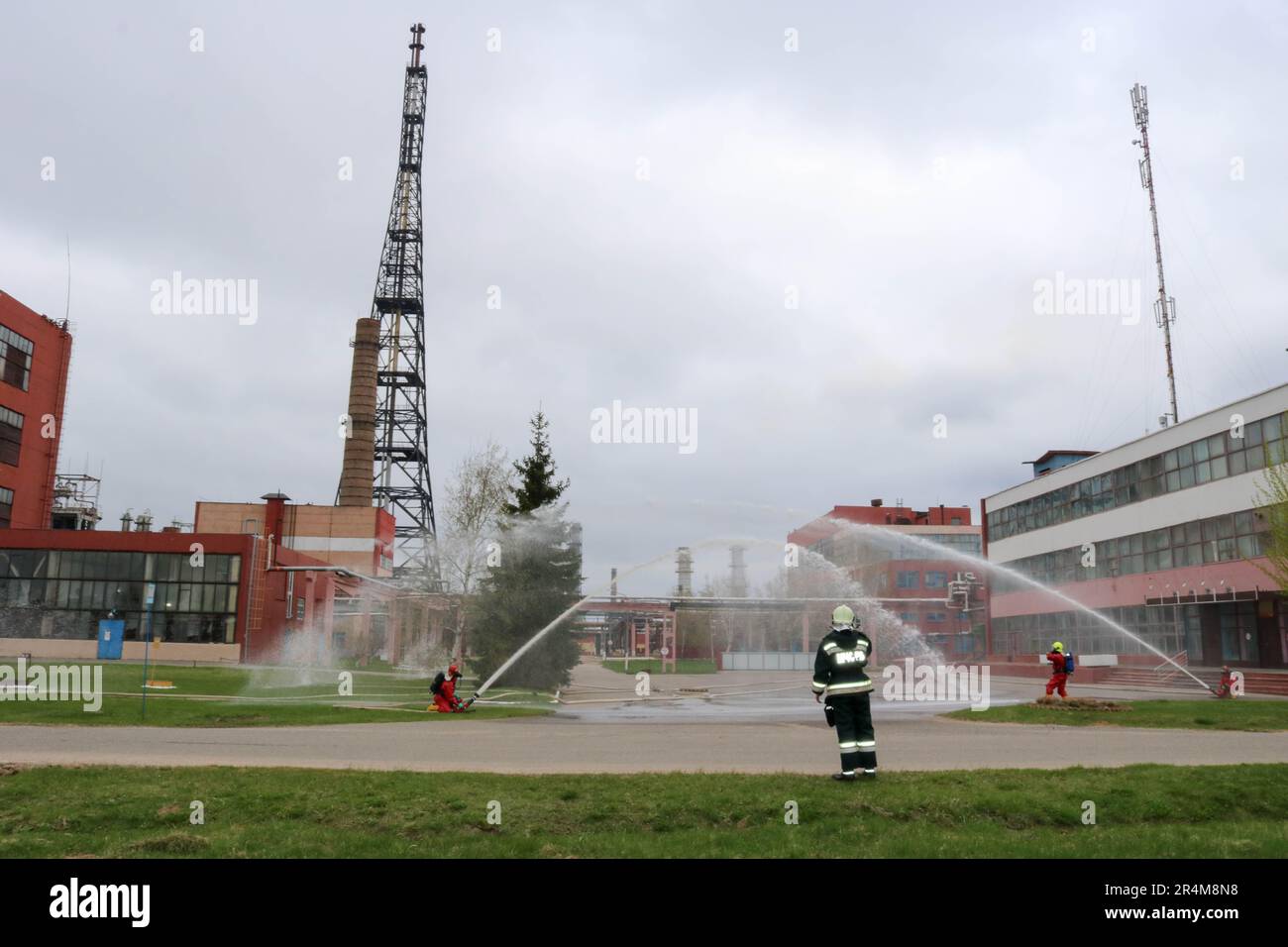 Professionelle Feuerwehrleute in orangefarbenen feuerfesten Anzügen in weißen Helmen mit Gasmasken testen Feuerlöschschläuche und Feuerwaffen, um einen Brand zu löschen Stockfoto