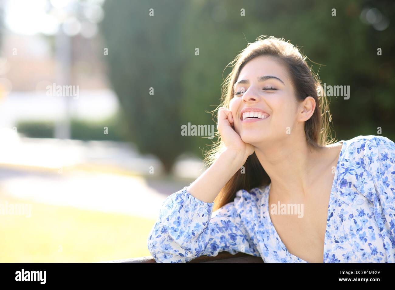 Eine glückliche Frau, die lacht und auf einer Bank im Park sitzt Stockfoto