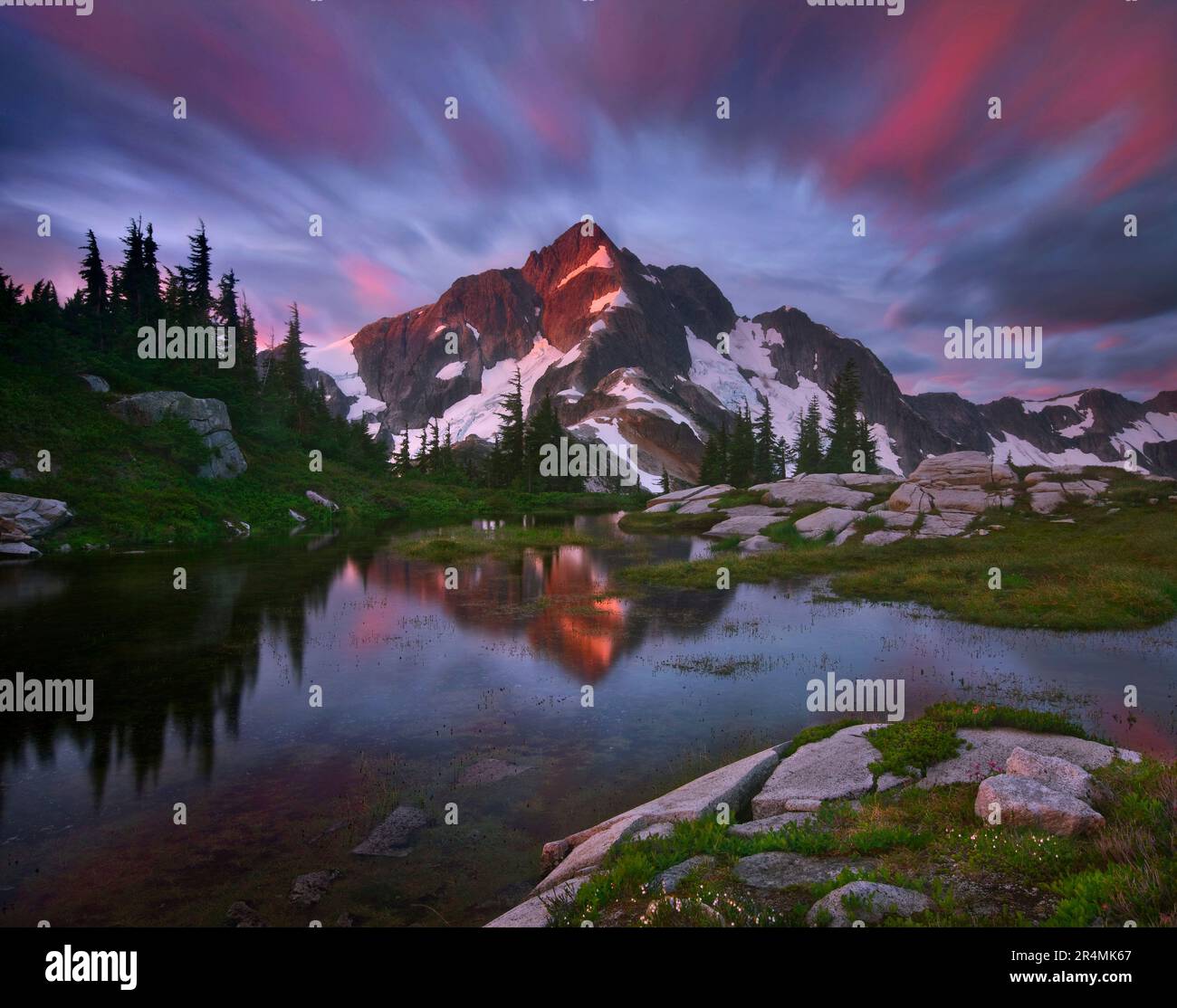 Ein atemberaubender Blick auf den Sonnenaufgang zum Whatcom Peak im North Cascades National Park wurde mit einer langen Exposition aufgenommen, die Wolkenbewegung und den Gipfel vervollständigt. Stockfoto