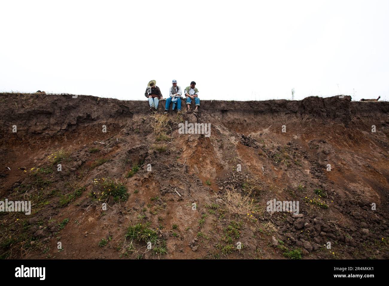 Drei Männer sitzen zusammen auf einem Kamm mit Blick auf einen Krater nach dem Erdbeben in Chile. Stockfoto