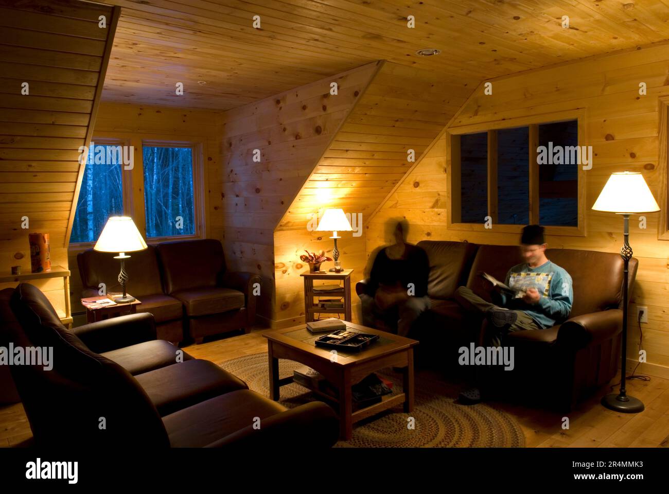 Zwei Männer entspannen sich abends auf einem Ledersofa im Poplar Stream Hut of Maine Huts and Trails. Maine, Neuengland. Stockfoto