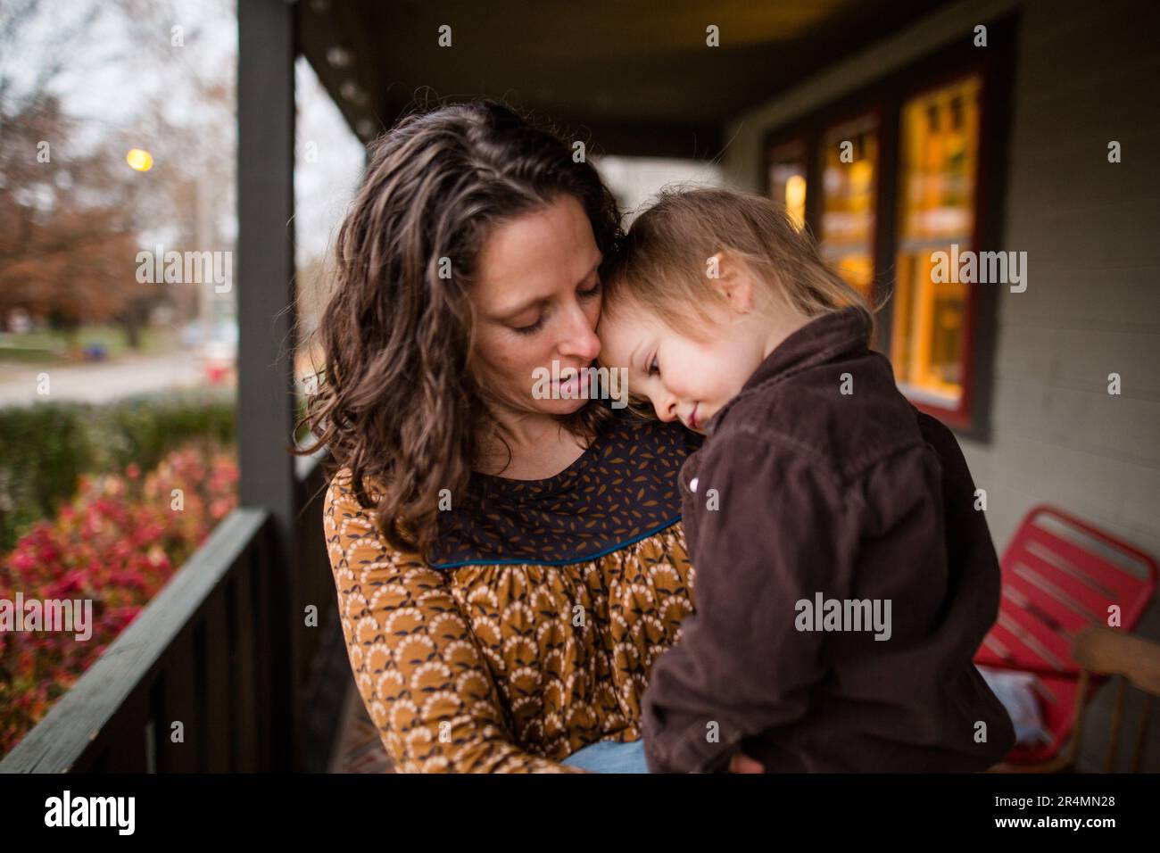 Eine Mutter hält ihr Kind auf der Veranda und legt seinen Kopf sanft auf seine Stockfoto