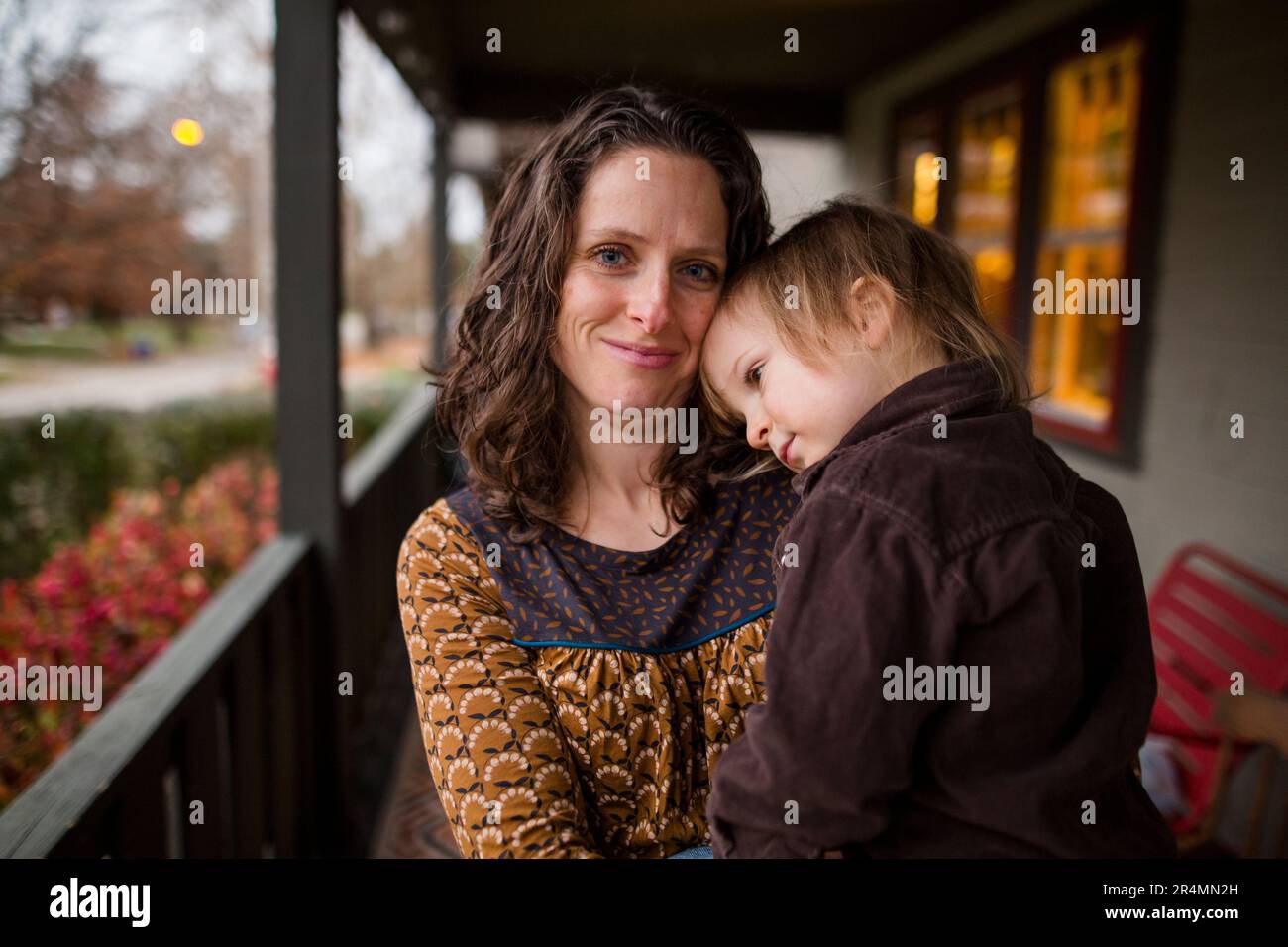 Eine lächelnde mutter steht draußen mit einem kleinen Kind in ihren Armen Stockfoto