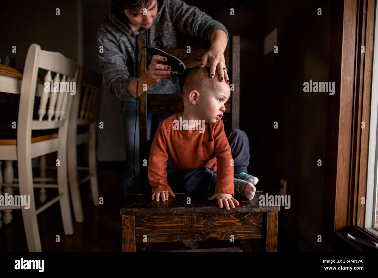 Mom schneidet jungen Jungs zu Hause die Haare, sitzt auf einem Stuhl und sieht weg Stockfoto