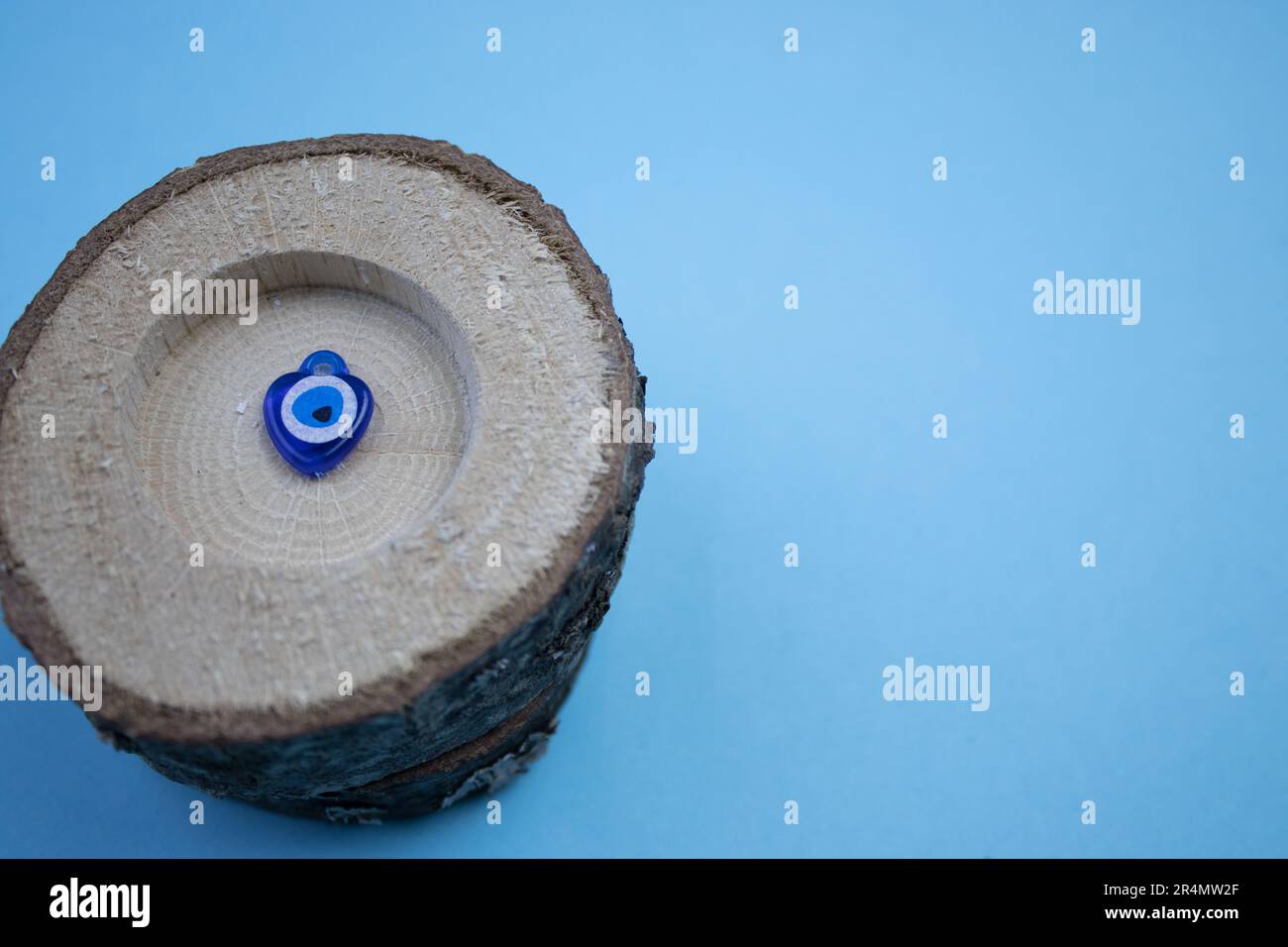 Der kleine Baumstamm und die böse Augenperle darin, fotografiert von oben, platziert am Rand des blauen Hintergrunds. Stockfoto