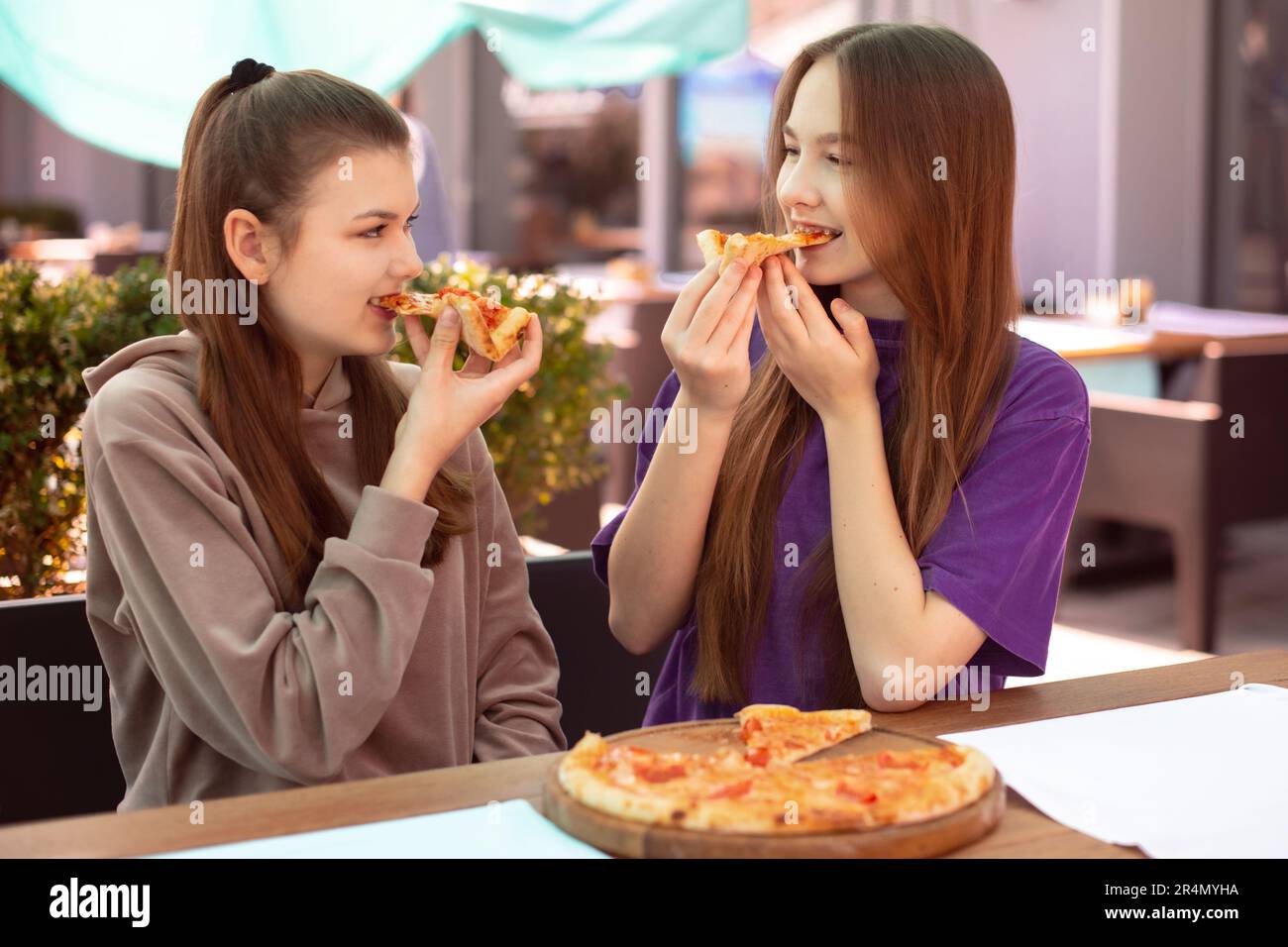 Zwei Teenager essen Pizza im Café draußen nach dem Unterricht. Zwei Freunde Teilen Sich Pizza Stockfoto