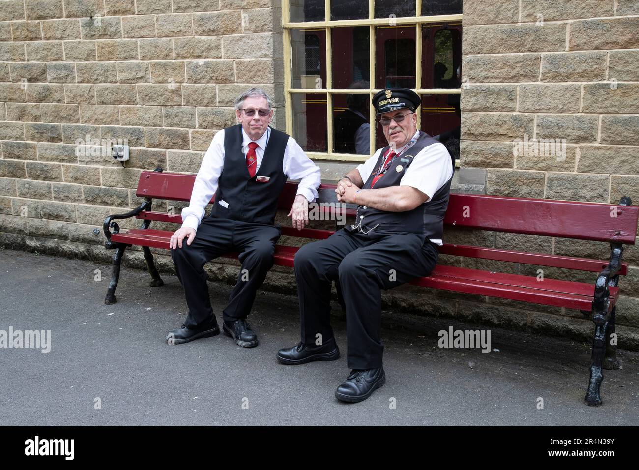 Zwei ehrenamtliche Mitarbeiter sitzen auf einer Bank der Keighley und Worth Valley Railway am Bahnhof Oxenhope Stockfoto