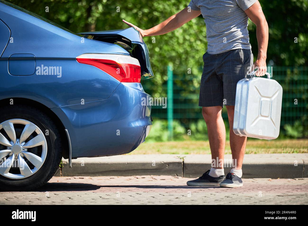 Ein Mann, der einen Kanister mit Benzin aus dem Kofferraum rausholt. Freigestellte Ansicht eines männlichen Erwachsenen, der die Zisterne mit Benzin herausnimmt, um sein blaues Auto aufzutanken. Stockfoto