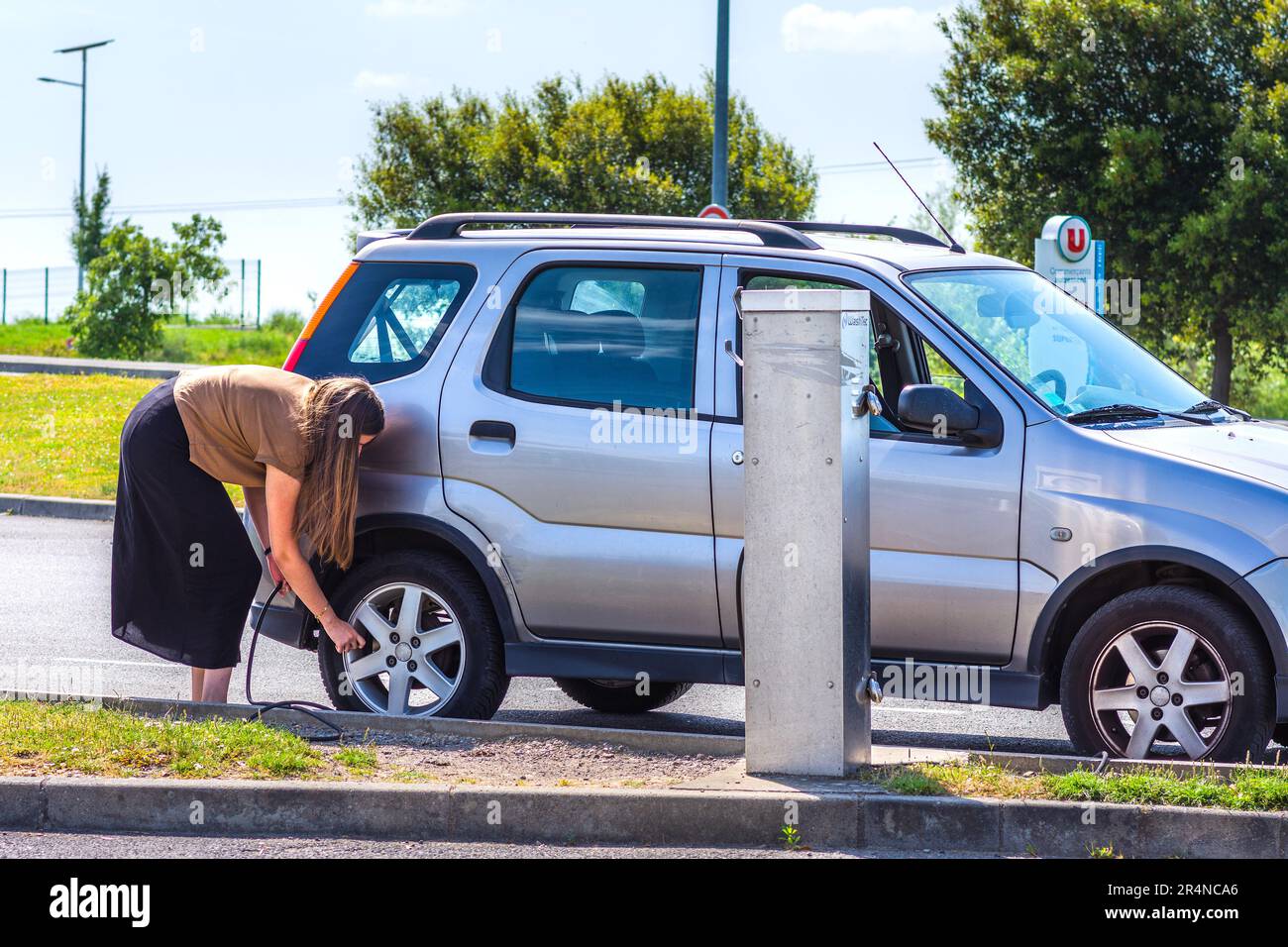 Junge Frau, die den Reifendruck auf dem Garagenplatz prüft - Loches, Indre-et-Loire (37), Frankreich. Stockfoto