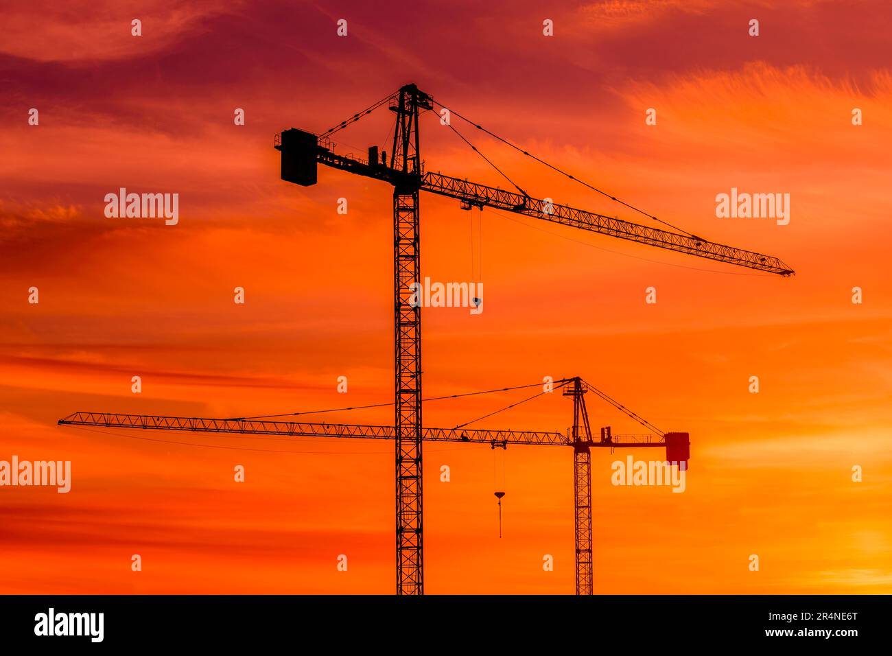 Silhouette von Baukränen vor dem leuchtend orangefarbenen Sonnenuntergangshimmel, Industriemaschinen und technischen Geräten Stockfoto