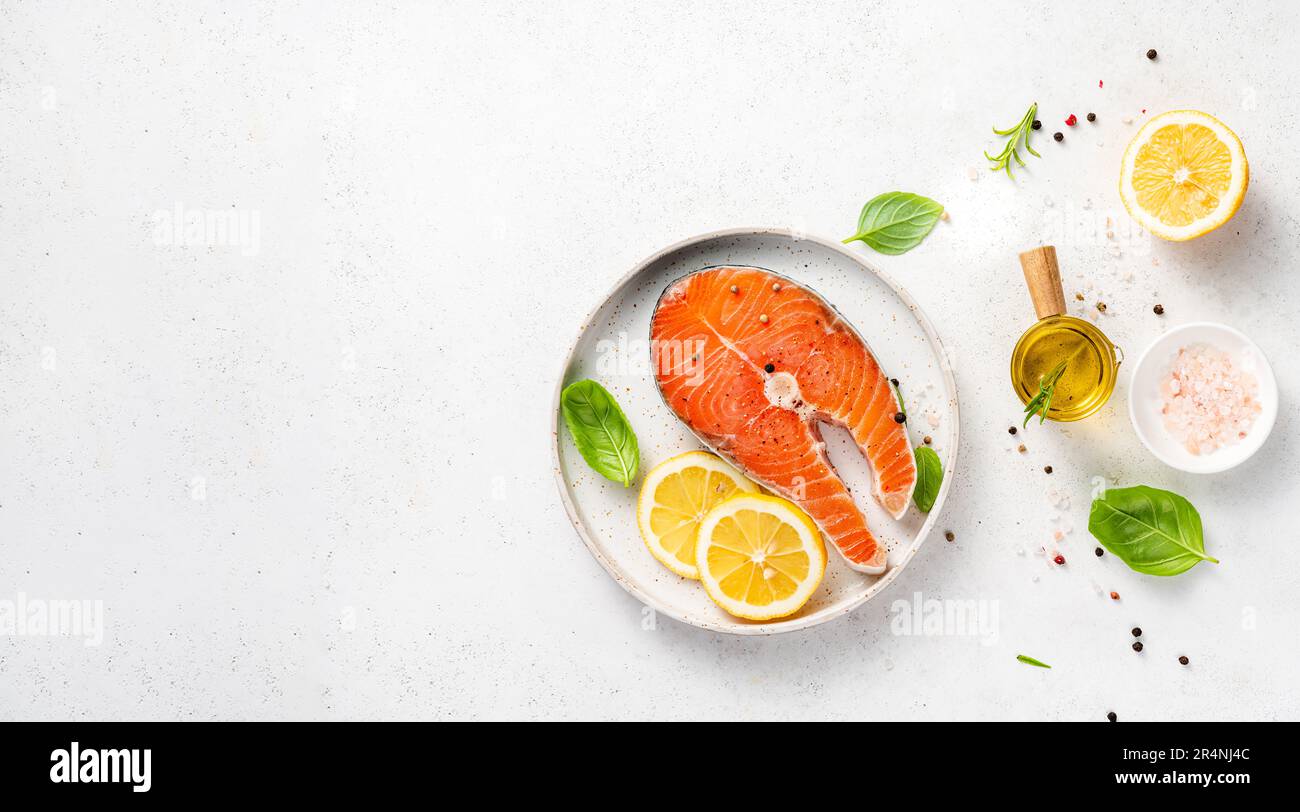 Frische rohe Lachssteaks mit Gewürzen, Zitronen und rosa Salz auf weißem Teller. Draufsicht auf Fische mit Kopierbereich. Keto-Rezept. Stockfoto