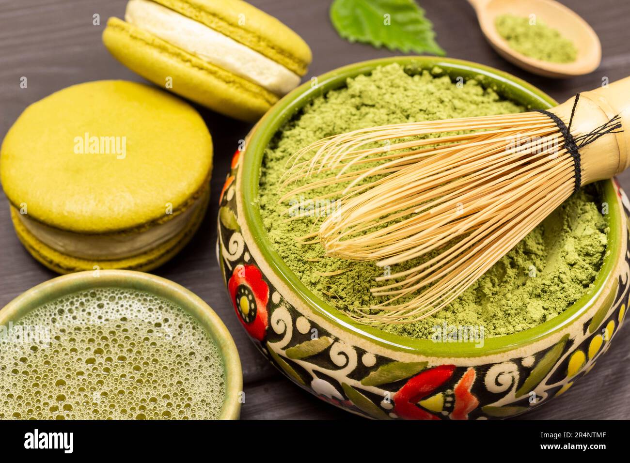 Bambus-Schneebesen in einer Schüssel mit Matcha-Pulver. Grüner Matcha-Tee und Makkaroni-Kuchen. Schließen Stockfoto