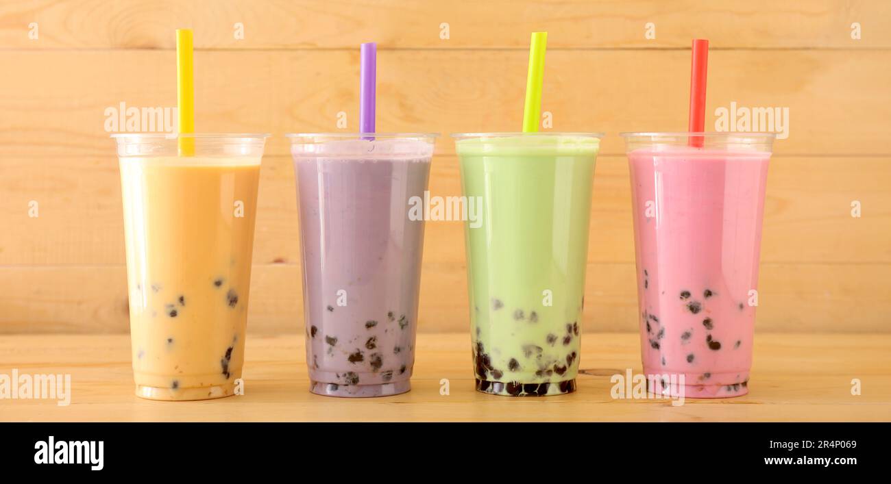 Plastikbecher mit verschiedenen leckeren Bubble Tea auf Holzhintergrund Stockfoto