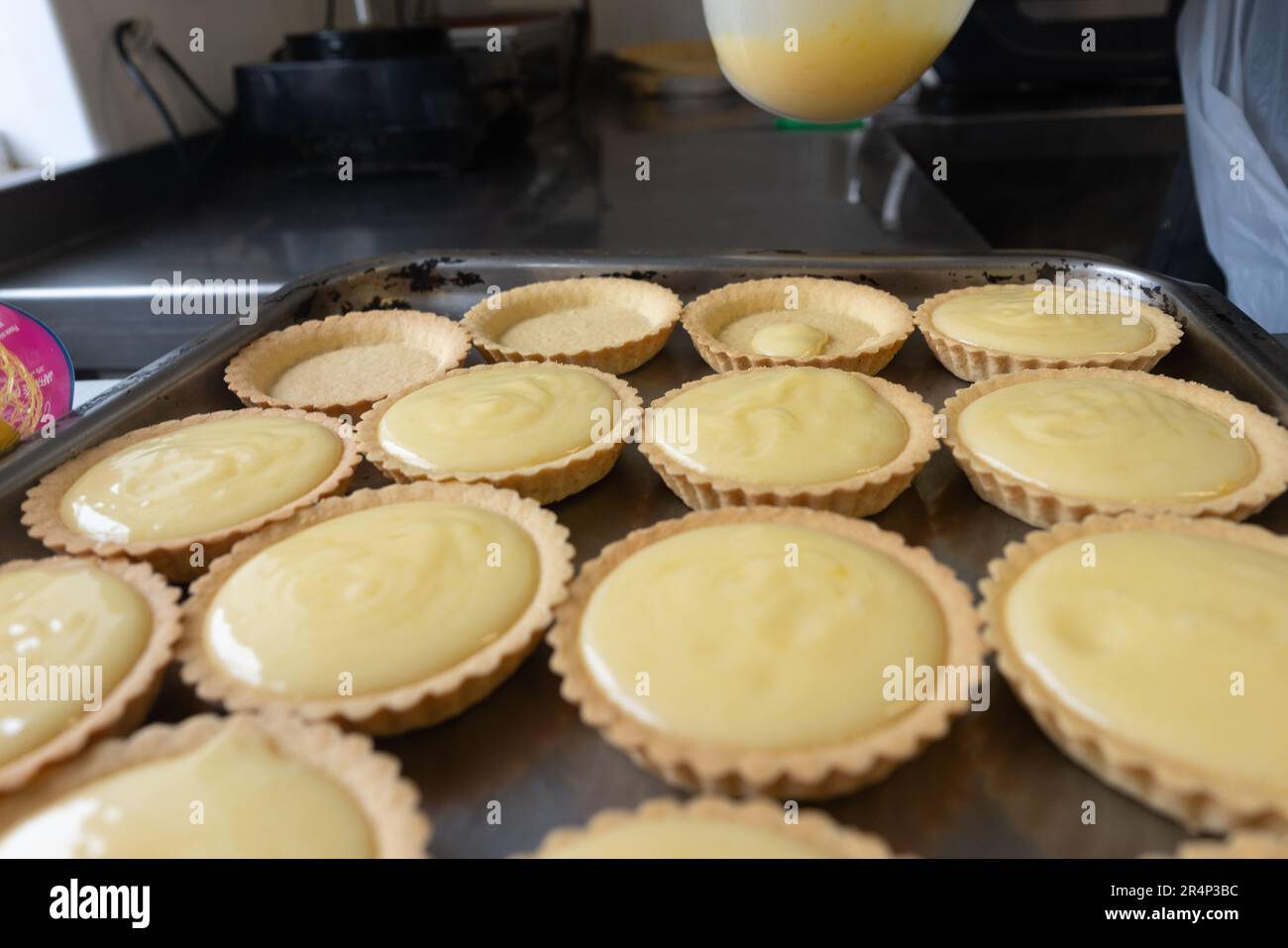 Lassen Sie sich verwöhnen von Zitronentörtchen, die perfekt auf einem Metalltablett mit einer kurzen, butterigen Teigkruste präsentiert werden. Stockfoto