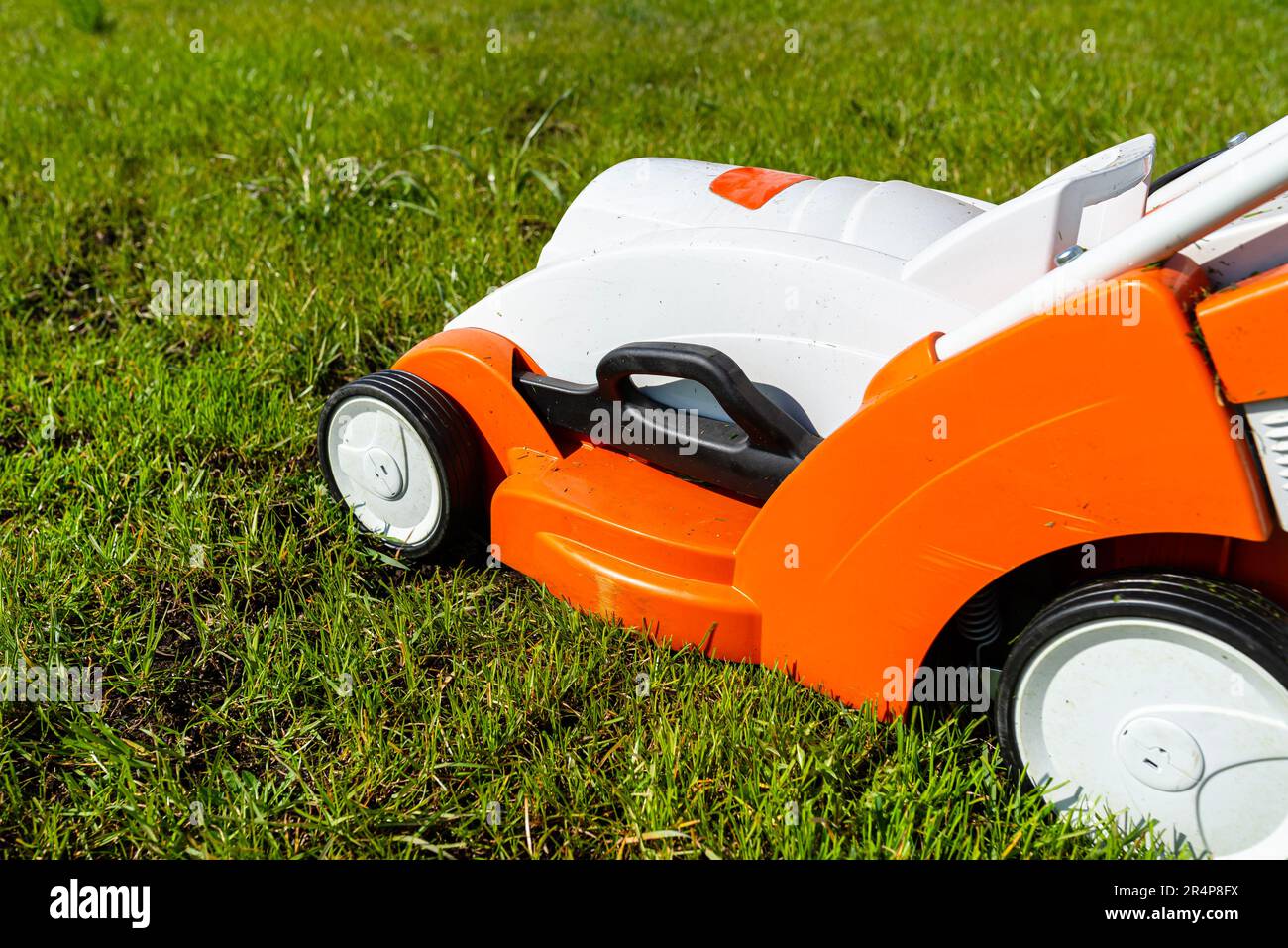 Ein kleiner, motorisierter Elektromäher steht auf dem Rasen und ist orange gefärbt. Stockfoto