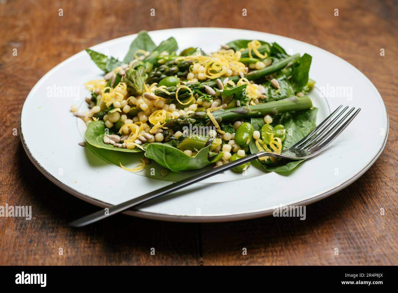 Teller mit einem hausgemachten veganen Couscous-Salat im Frühling mit grünem Spargel, Favabohnen und Baby-Spinat. Stockfoto
