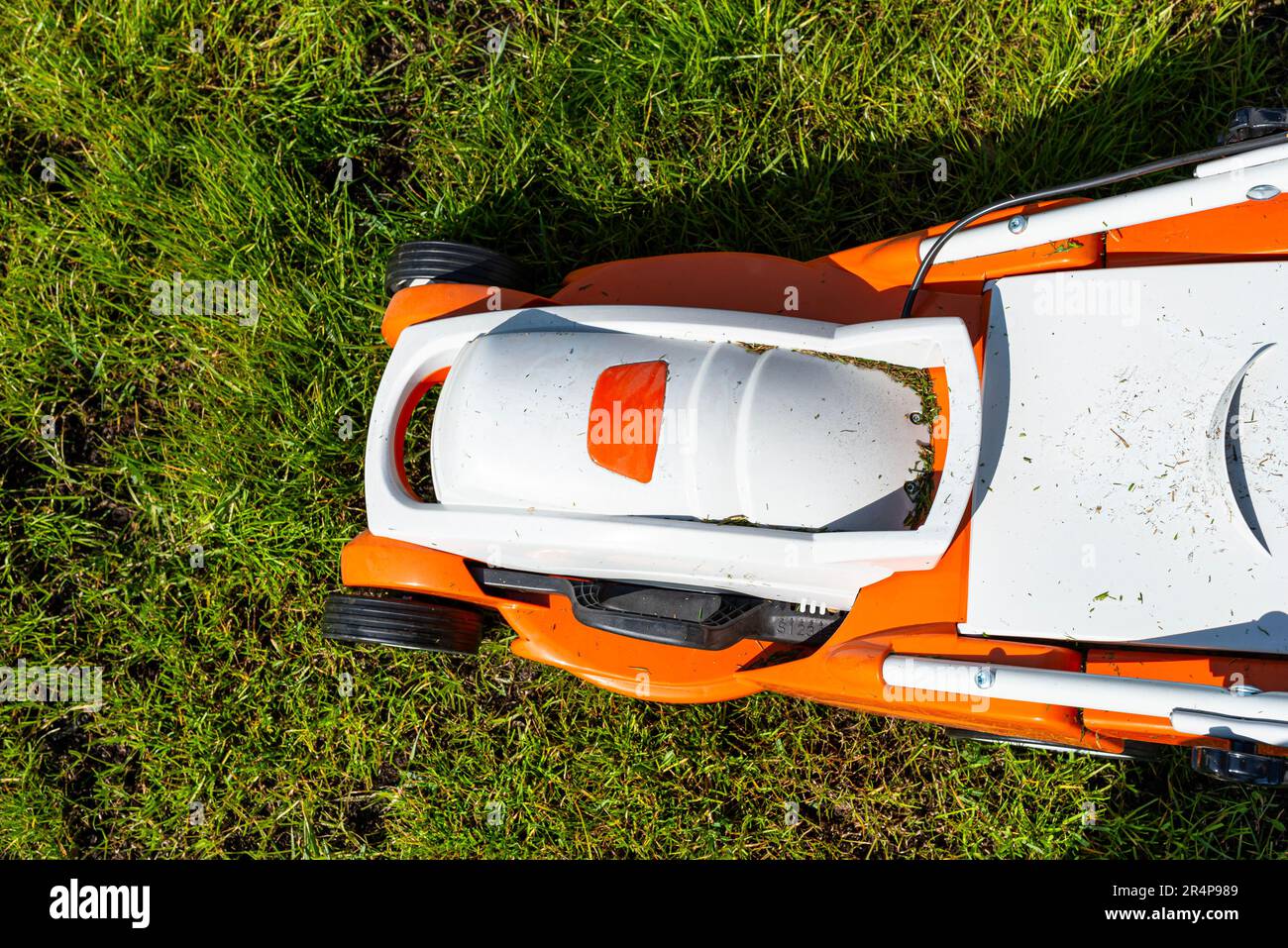 Ein kleiner, motorisierter Elektromäher steht auf dem Rasen und ist orange gefärbt. Stockfoto