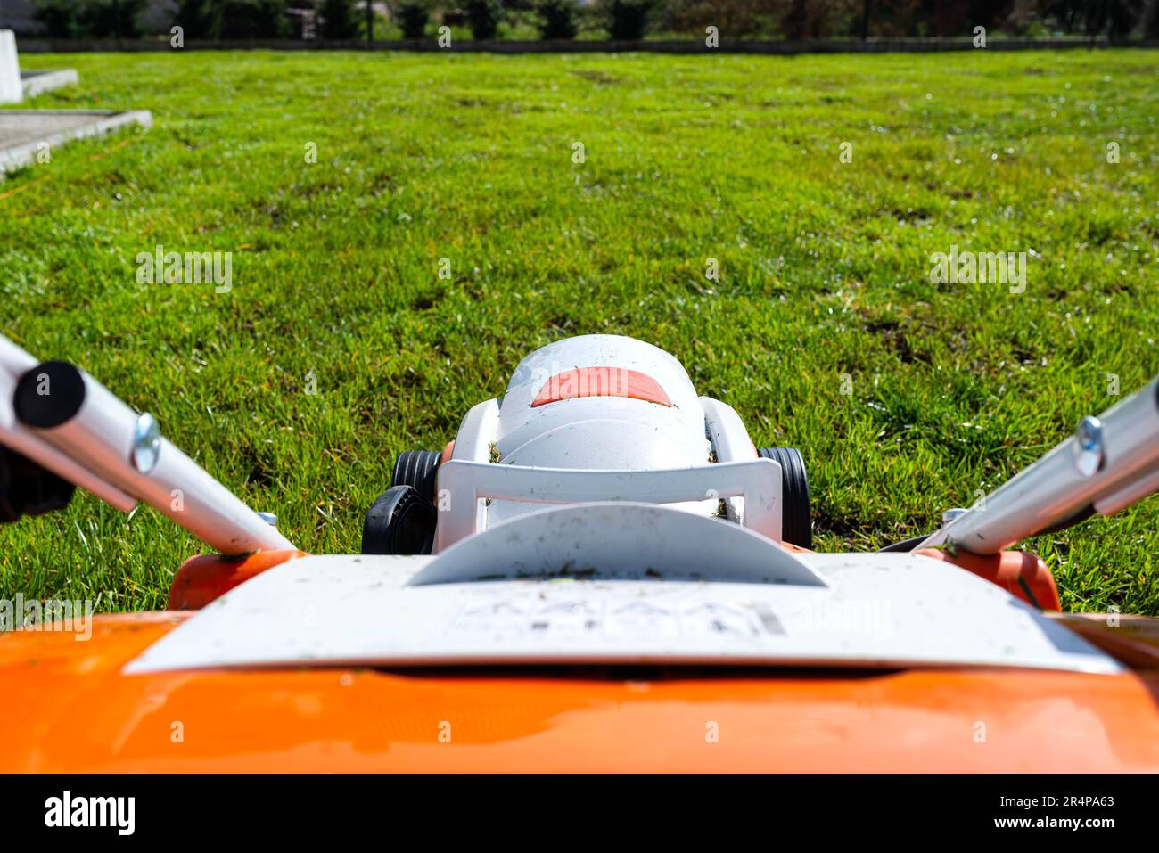 Ein kleiner, motorisierter Elektromäher steht auf dem Rasen und ist orange gefärbt. Stockfoto