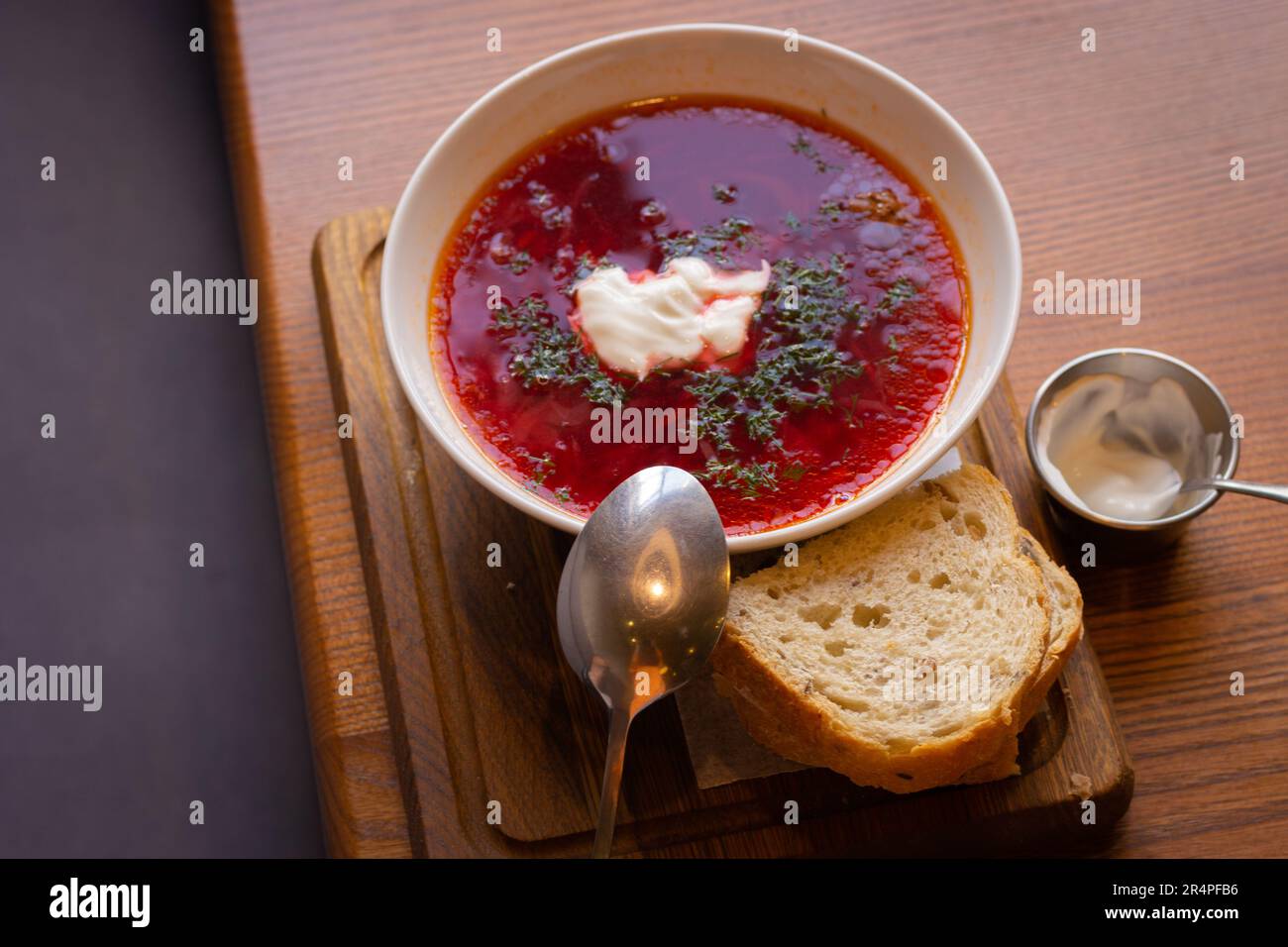 Ukrainischer Borsch mit Brot auf Holztisch. Rote Suppe mit Sahne und Brot. Ukrainisches traditionelles Essen. Hausgemachter Borscht. Tomatensuppe zum Abendessen. Stockfoto