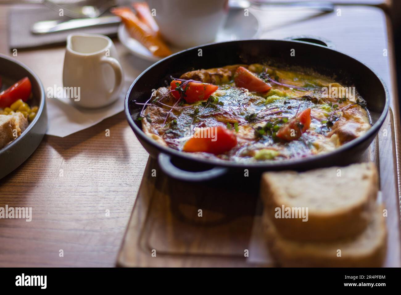 Spiegeleier mit Tomaten und Schinken in der Pfanne. Frühstückstisch serviert. Omelette mit Tomaten und Brot. Spanische Tortilla. Eier mit Pesto und Gemüse. Stockfoto