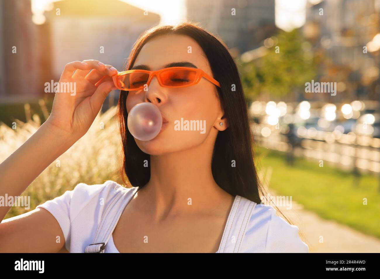 Schöne Frau mit Sonnenbrille, die draußen Kaugummi bläst Stockfoto