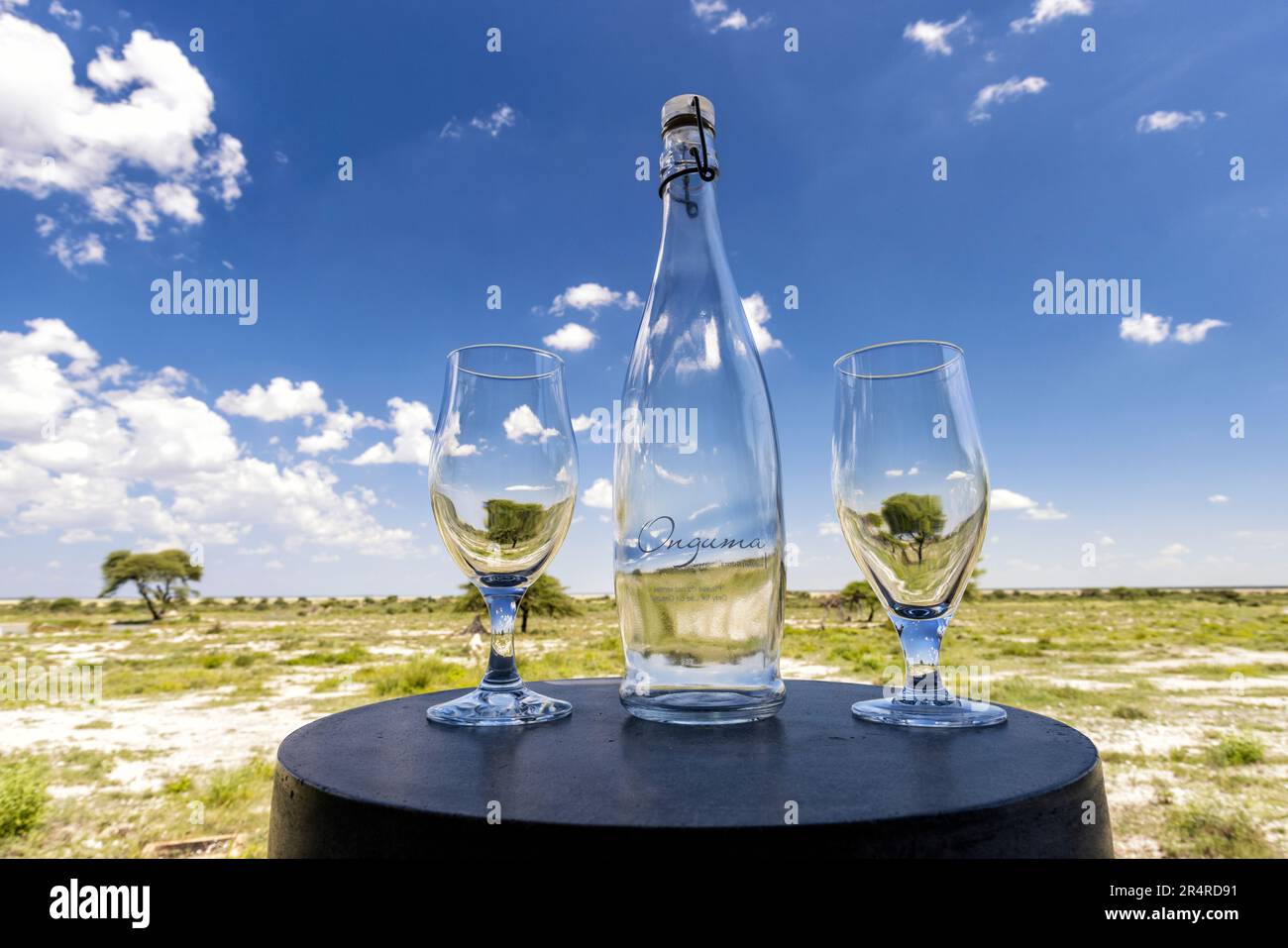 Nahaufnahme von Onguma Flasche und Gläsern mit Fisher's Pan im Hintergrund – Onguma The Fort, Onguma Game Reserve, Namibia, Afrika Stockfoto