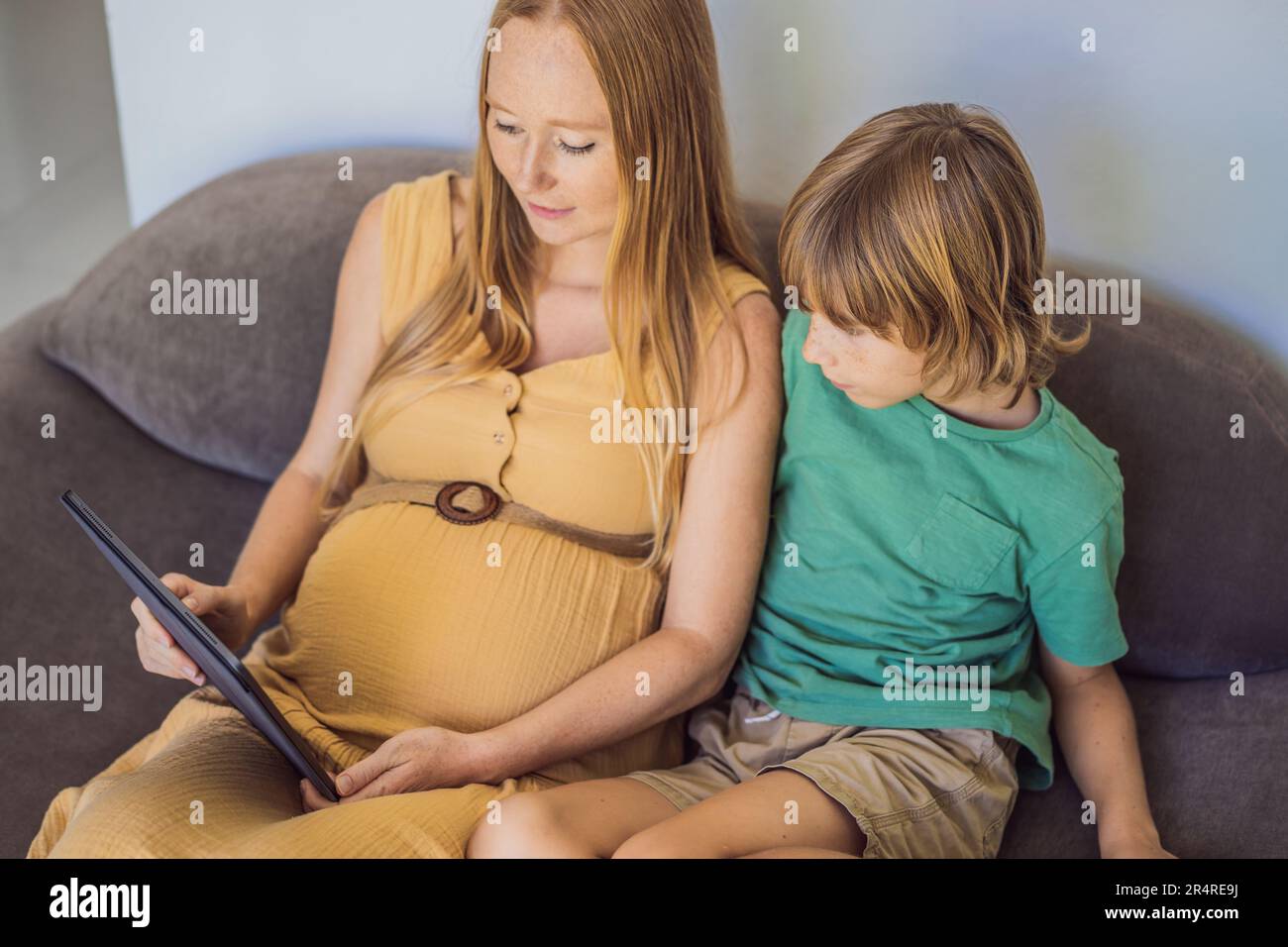 Schwangere mutter und Sohn sehen sich die Tablette an. Ein Buch lesen, einen Cartoon ansehen oder einen Videoanruf tätigen. Sehen Sie sich das Foto vom Ultraschall an Stockfoto