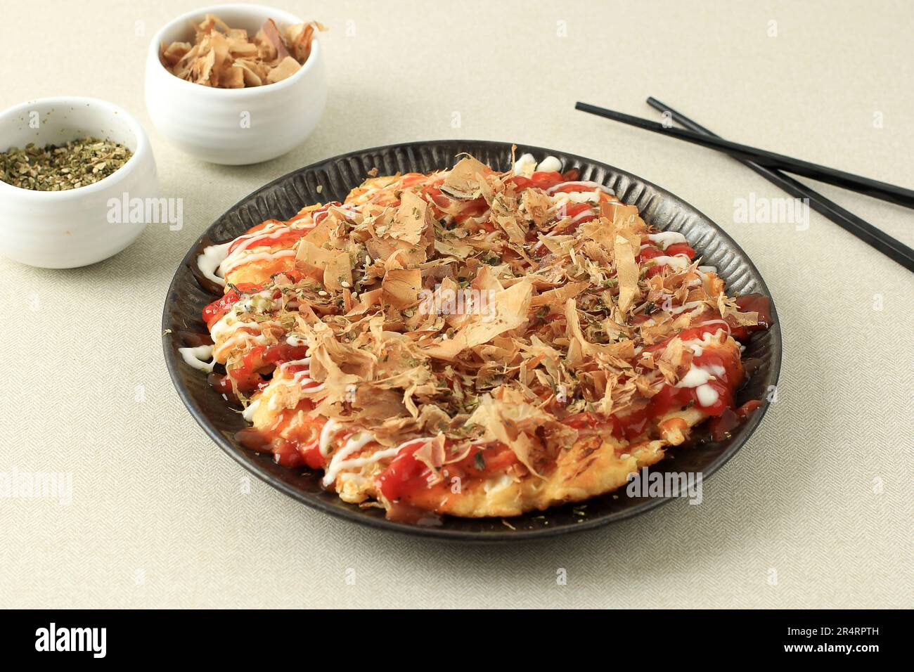 Japanisches Essen, Okonomiyaki, japanische Pfannkuchen, Garnierung mit Katsuobushi, Mayonaise, Chilisoße Stockfoto