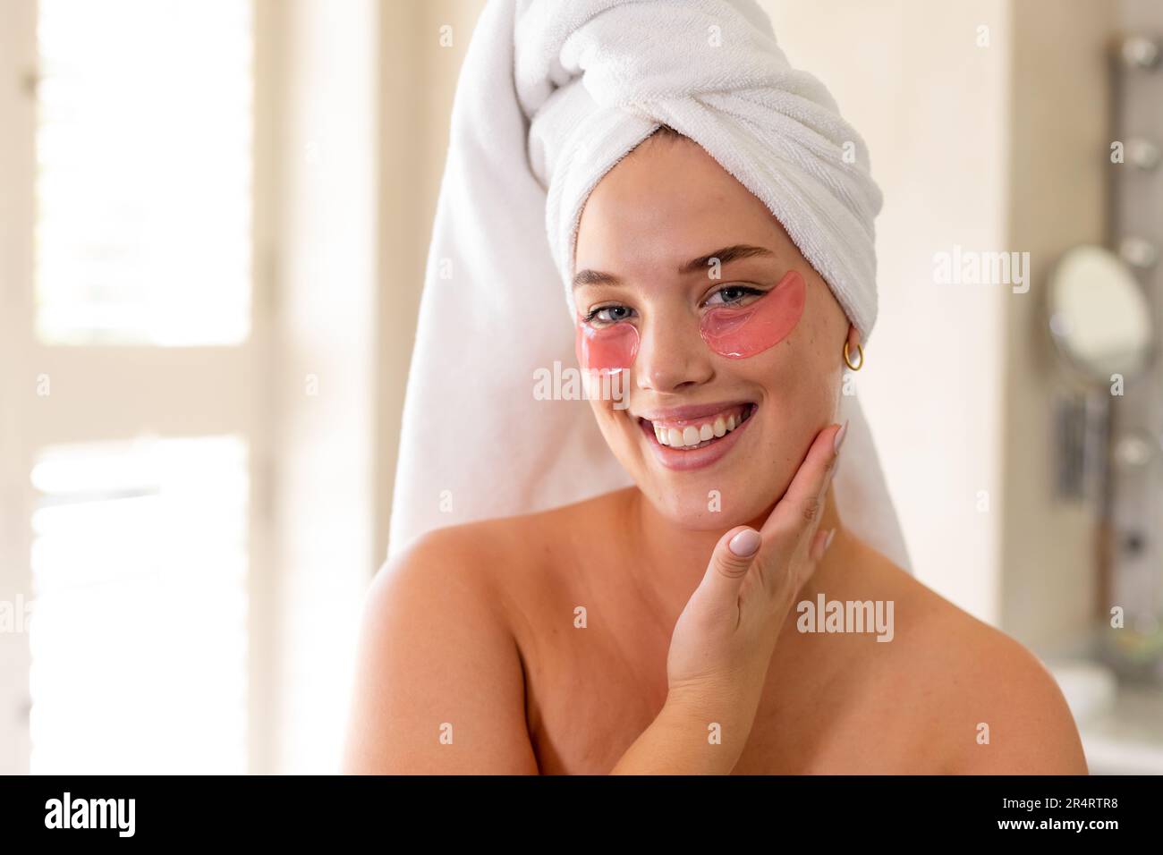 Lächelnde weiße Frau in Übergröße mit Handtuch am Kopf und roten Augenflecken unter den Augen Stockfoto