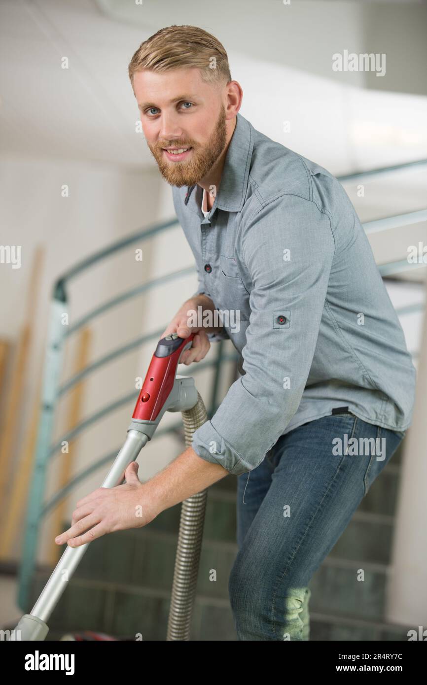 Ein hübscher Mann, der das Büro mit dem Staubsauger reinigt Stockfoto